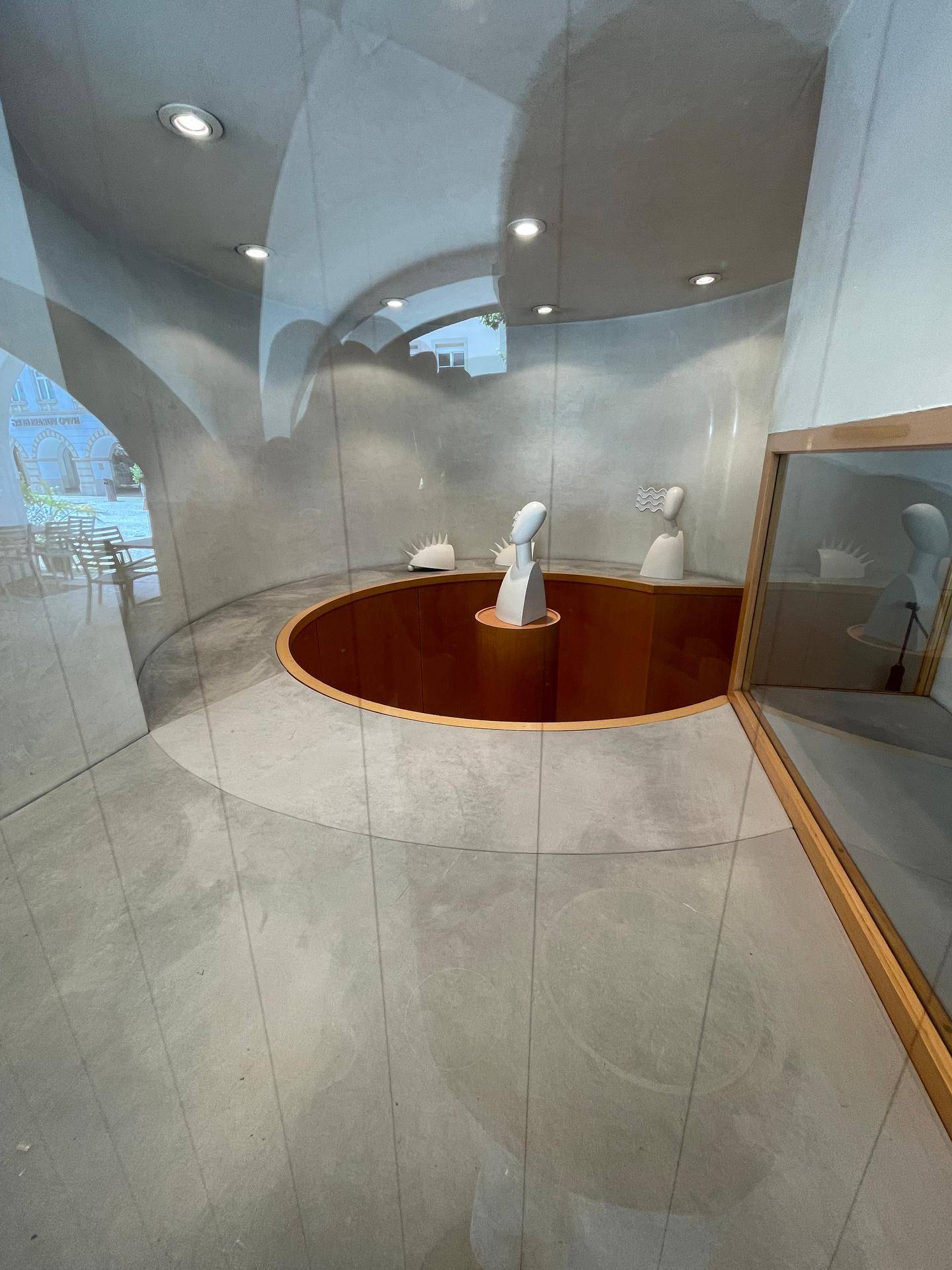 Runder Ausstellungsraum mit Betonboden, geschwungenen Wänden und modernen Präsentationsobjekten.