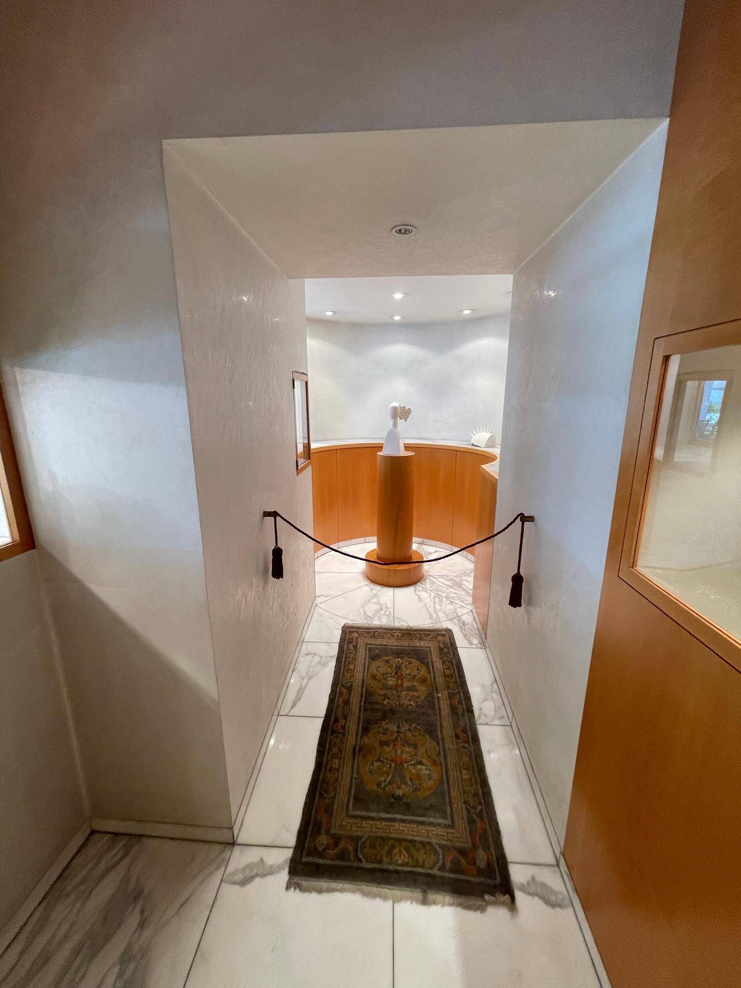 Heller Flur mit Marmorboden und einem dekorativen Teppich, der zu einem runden Ausstellungsbereich führt.