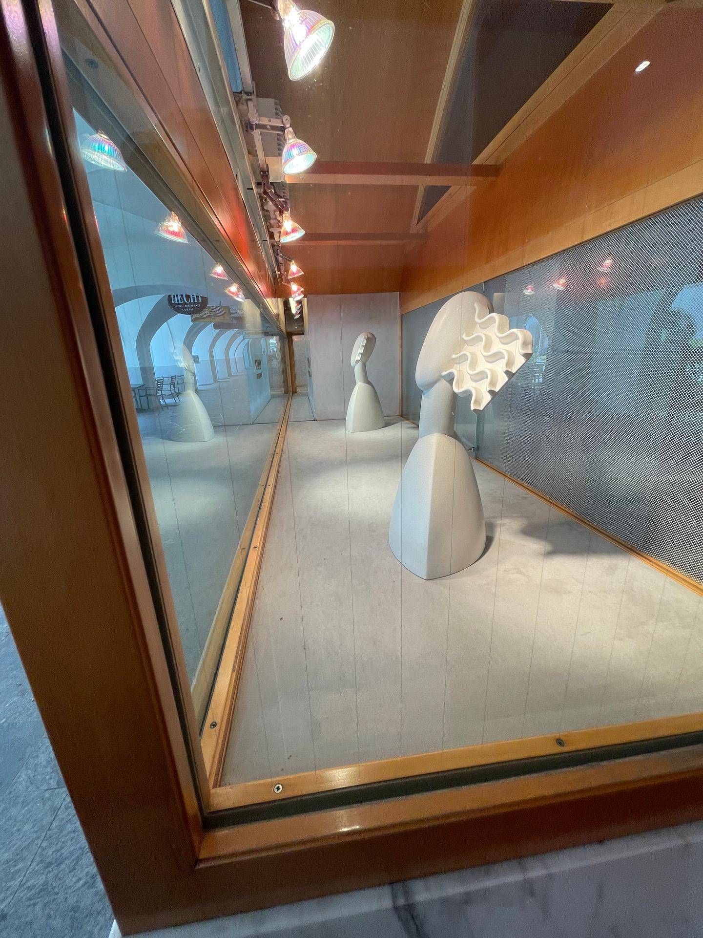 Schaufenster mit Ausstellungsstücken und Spiegelungen der Außenwelt, beleuchtet von Strahlern.