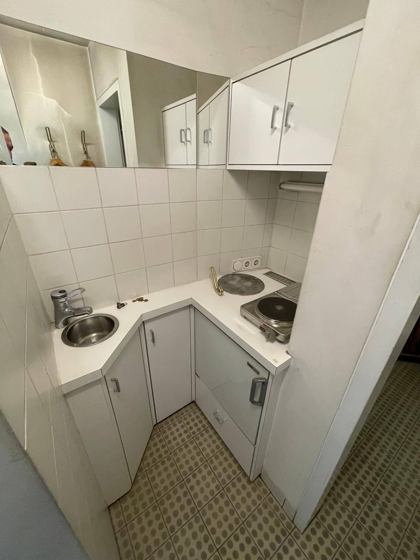 Kleine, funktionale Küchenzeile mit weißen Schränken, Spüle und Kochfeld, ideal für kompakte Räume.