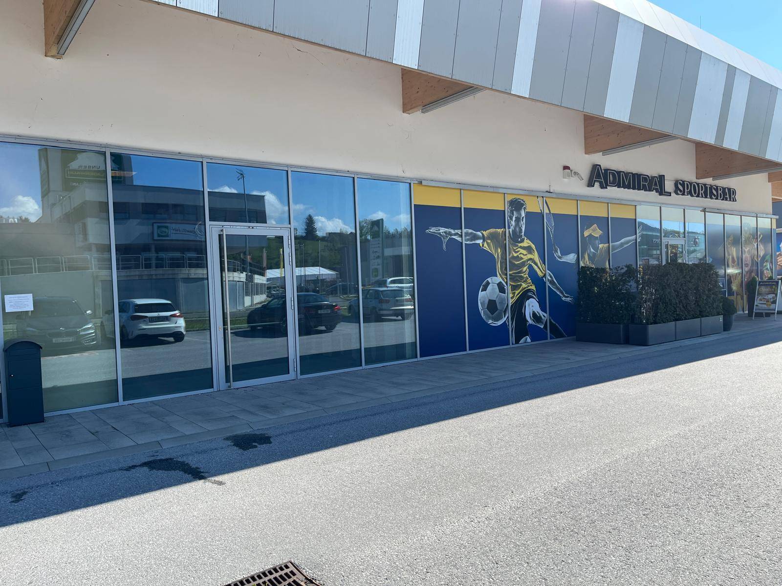 Außenansicht eines modernen Geschäftsgebäudes mit Glasfassade und Werbegrafik für eine Sportsbar.