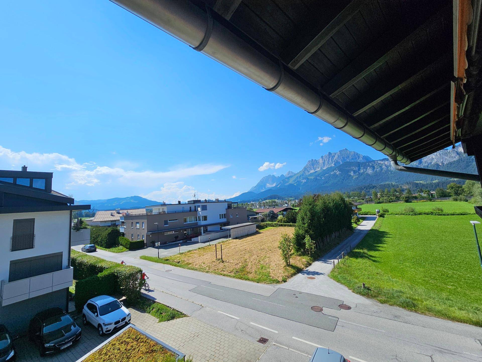 Weitläufiger Ausblick vom Balkon über die Wohngegend, grüne Wiesen und die beeindruckende Bergkulisse.