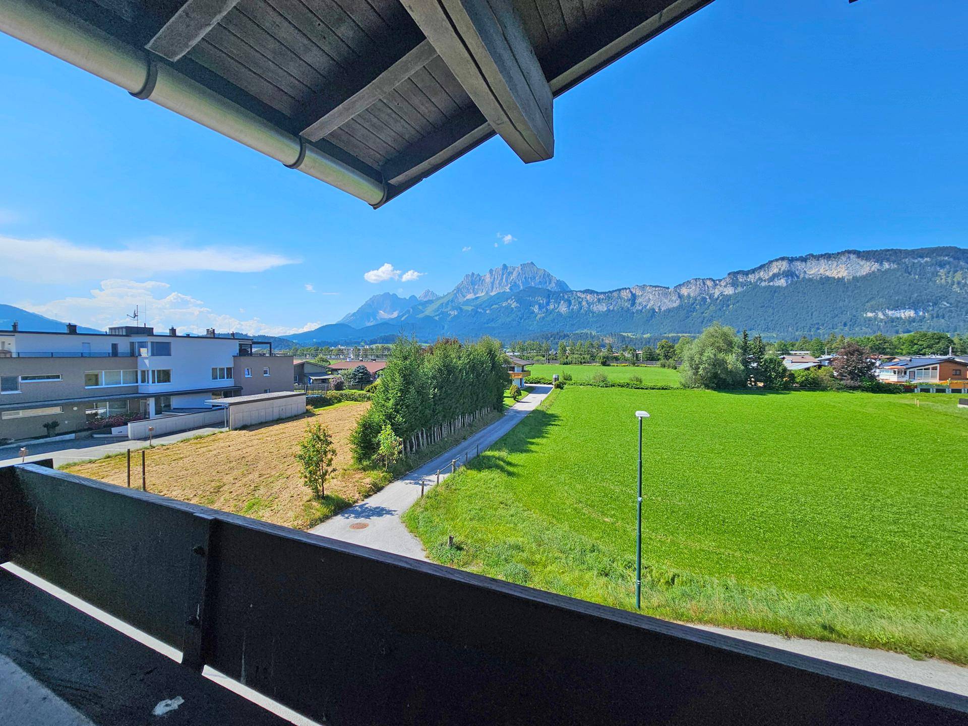 Sonniger Balkon mit freiem Blick auf weite grüne Wiesen und die imposanten Berge am Horizont.
