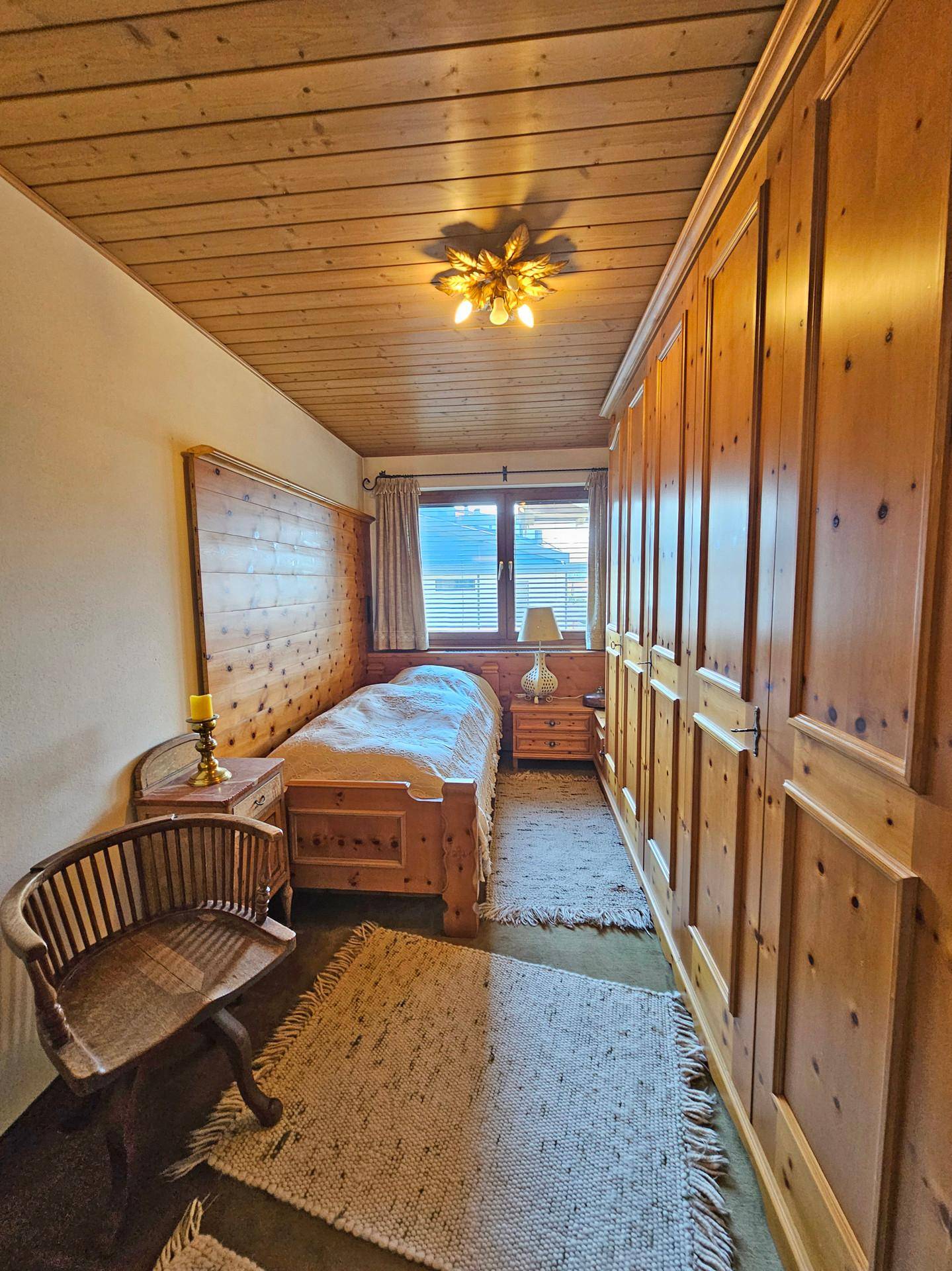 Schlafzimmer mit Einzelbett, Holztäfelung und integrierten Holzschränken entlang der Wand.