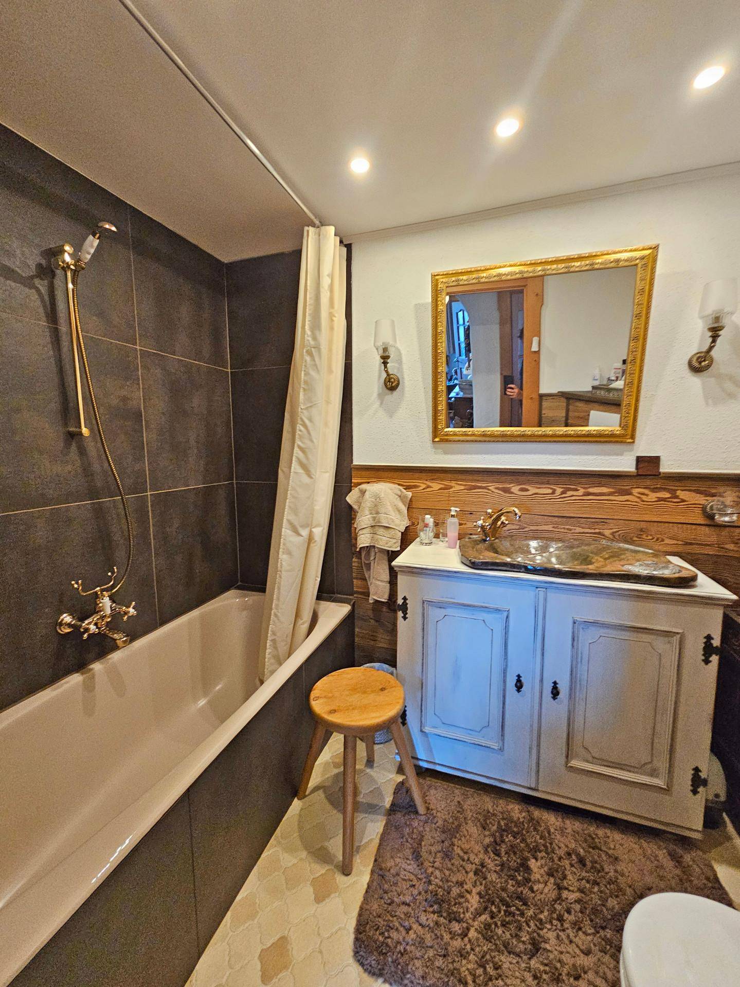 Badezimmer mit Badewanne, einem Waschtisch mit Holzbecken und einem verzierten Goldrahmen-Spiegel.