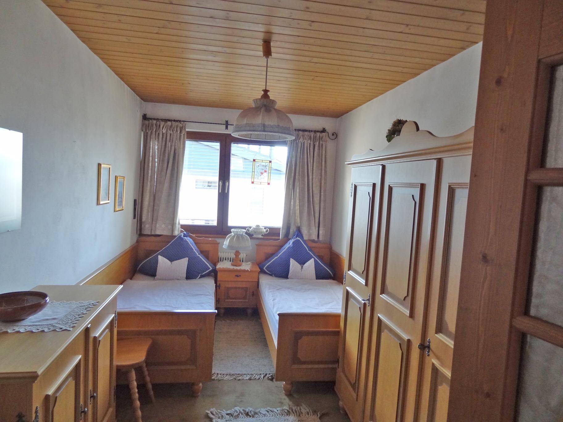 Helles Schlafzimmer mit zwei Einzelbetten, Holzdecke und einem traditionellen Kleiderschrank.