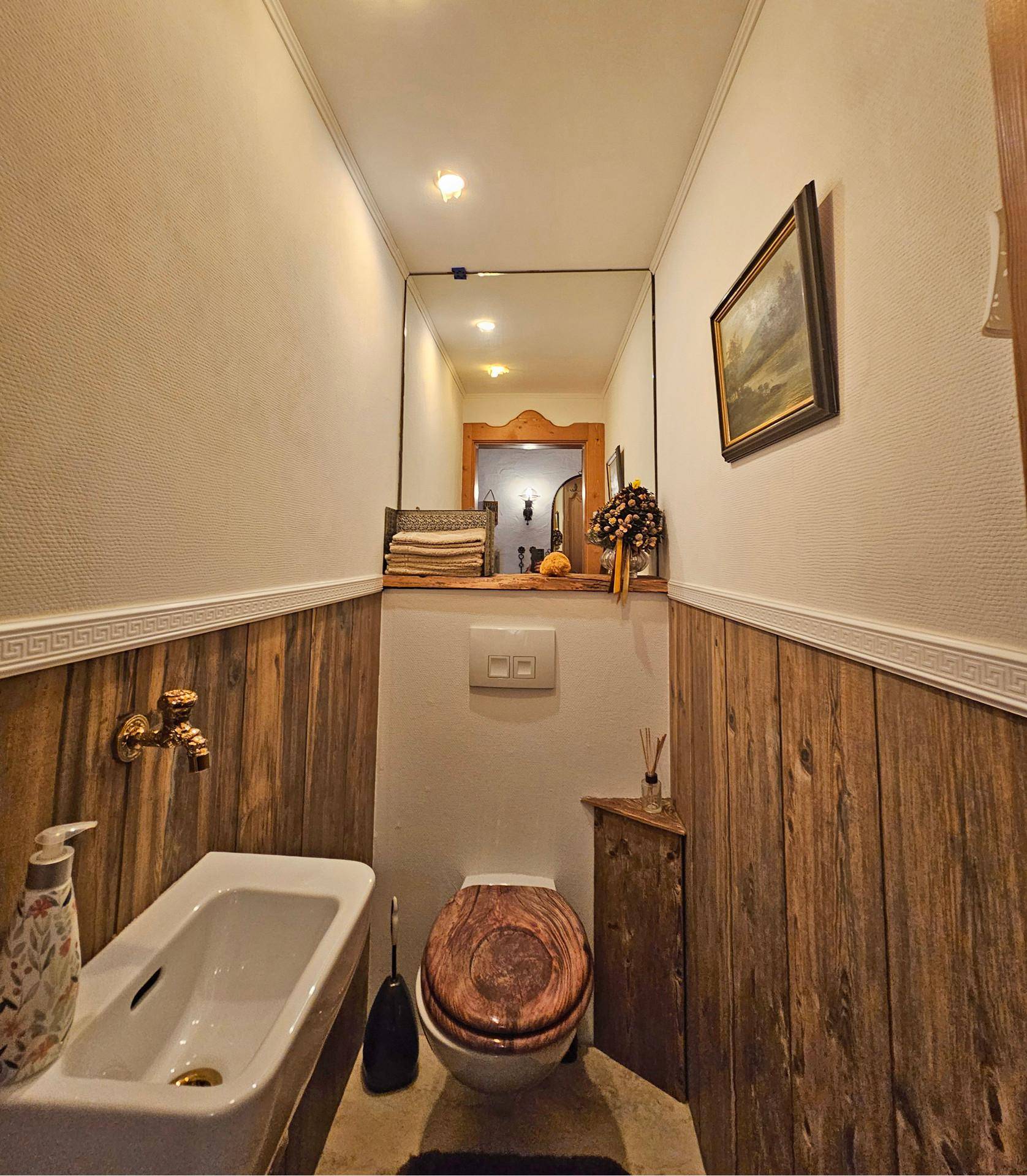 Gäste-WC mit wandhängender Toilette, kleinem Waschbecken und rustikaler Holzvertäfelung.