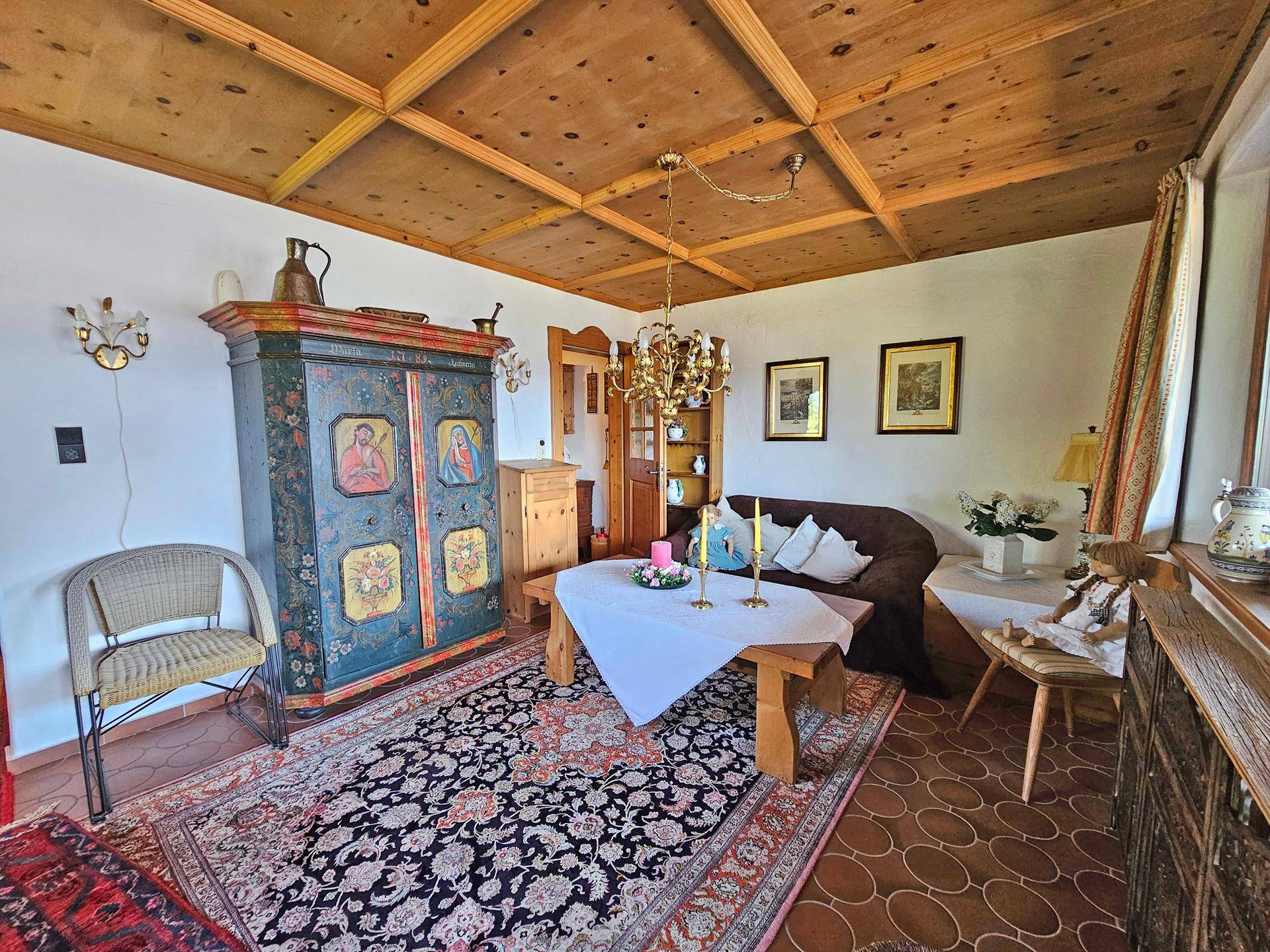 Traditionelles Wohnzimmer mit Holzbalkendecke, einem bemalten Schrank und einem orientalischen Teppich.