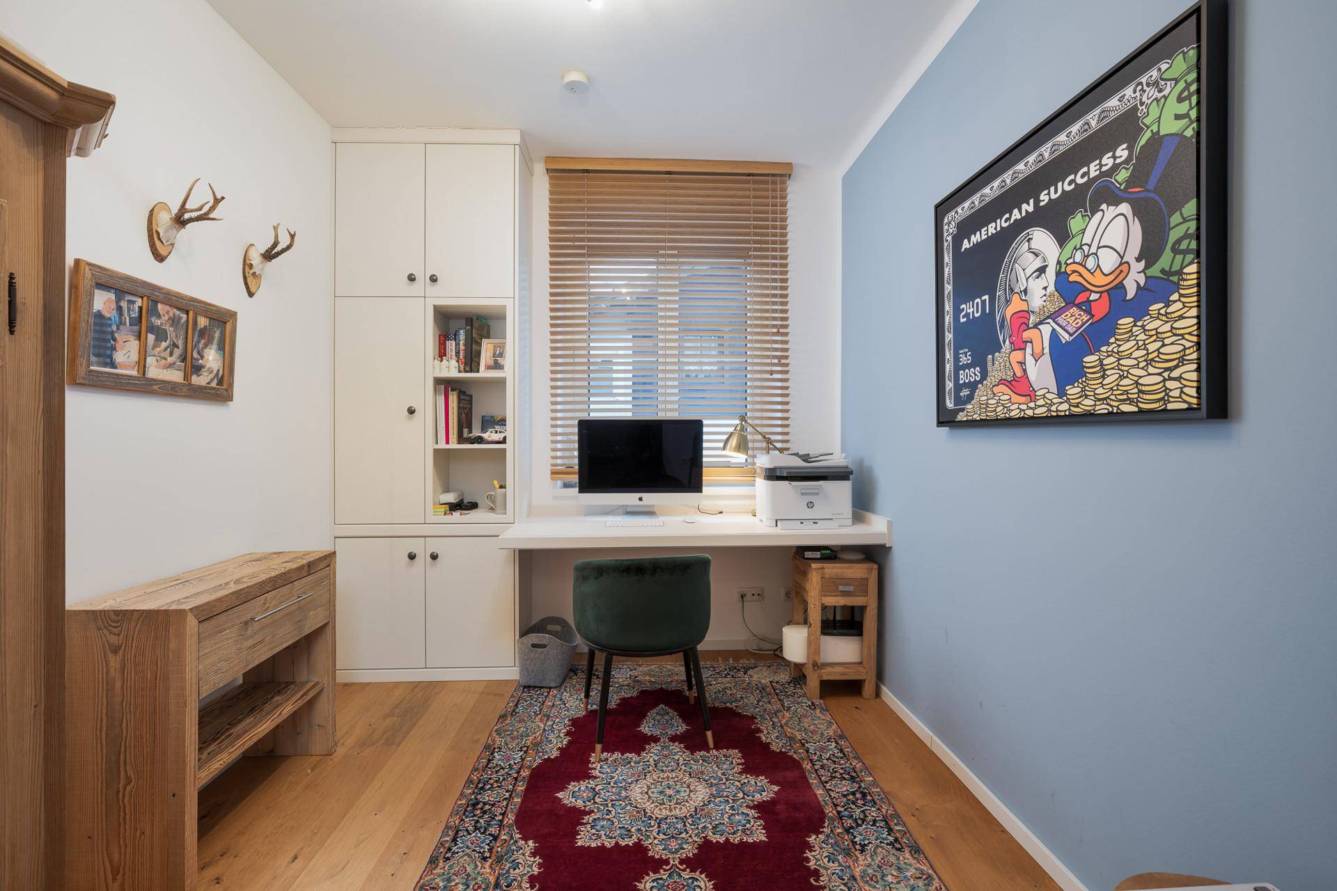 Helles Arbeitszimmer mit Einbauschränken, Holzboden und einem Fenster mit Jalousien.