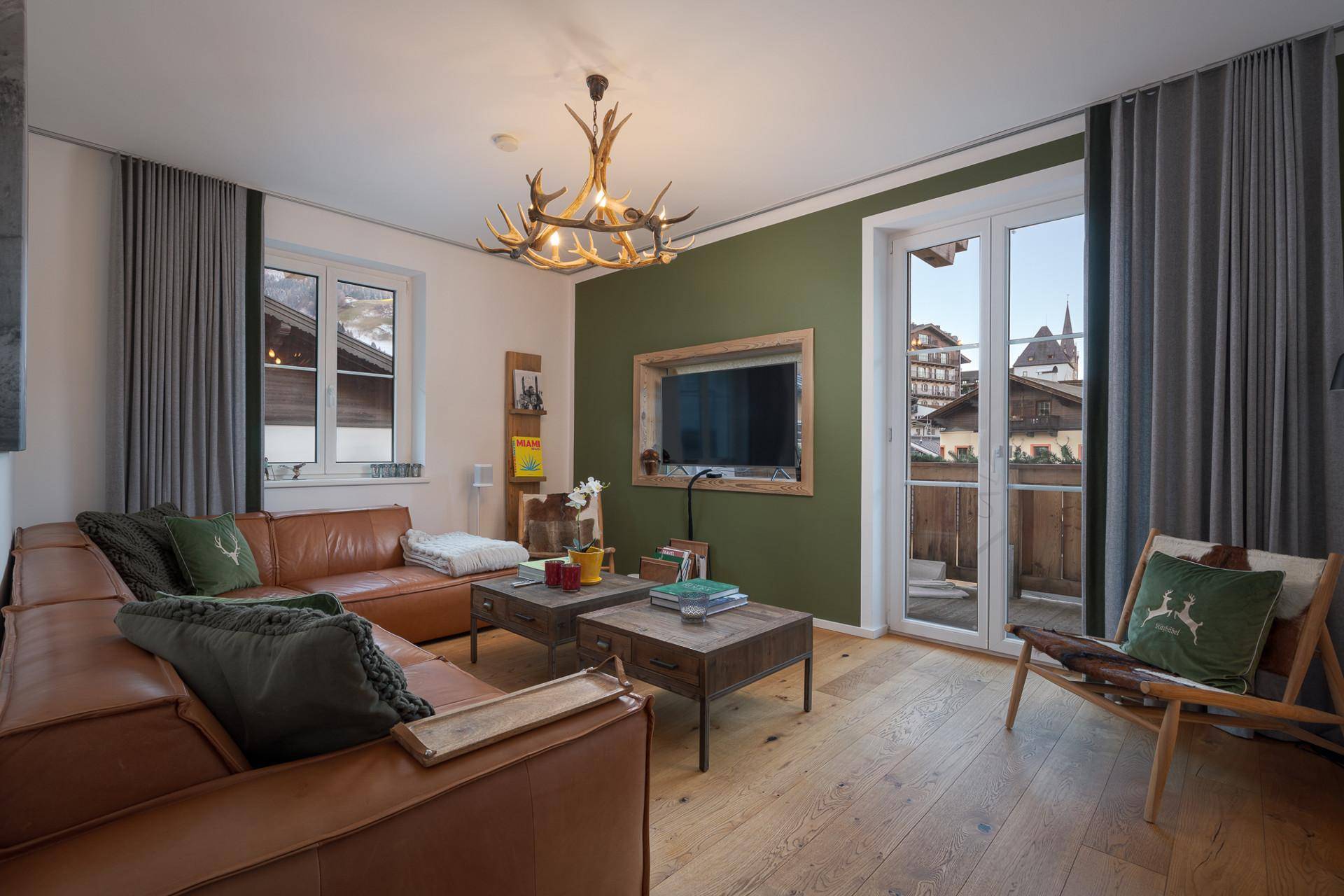 Gemütliches Wohnzimmer mit Ledersofa, Holzboden und Zugang zu einem Balkon mit Bergblick.