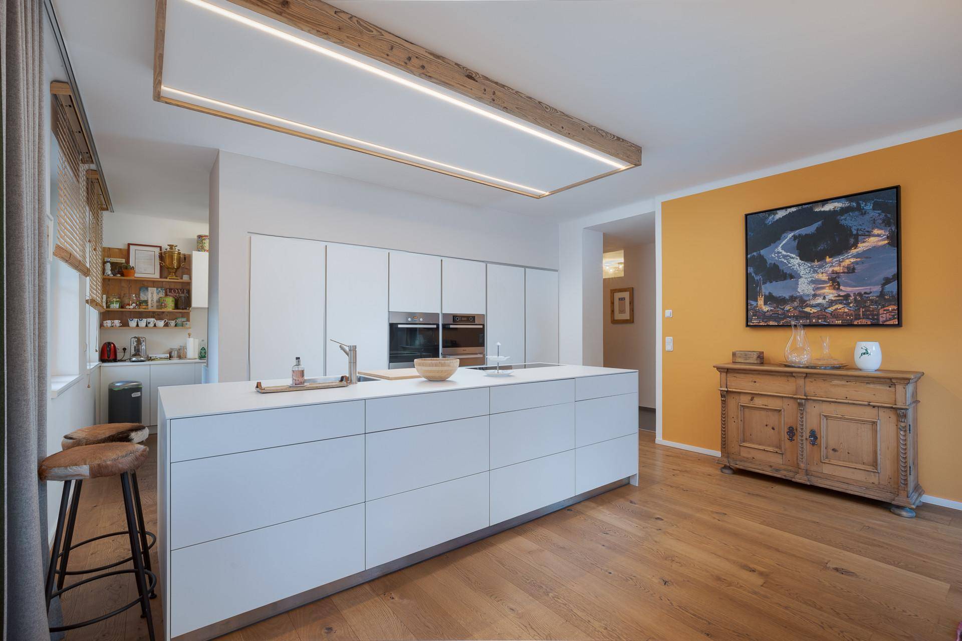 Moderne weiße Küche mit Kochinsel und Holzboden, offen zum Essbereich und Wohnzimmer.