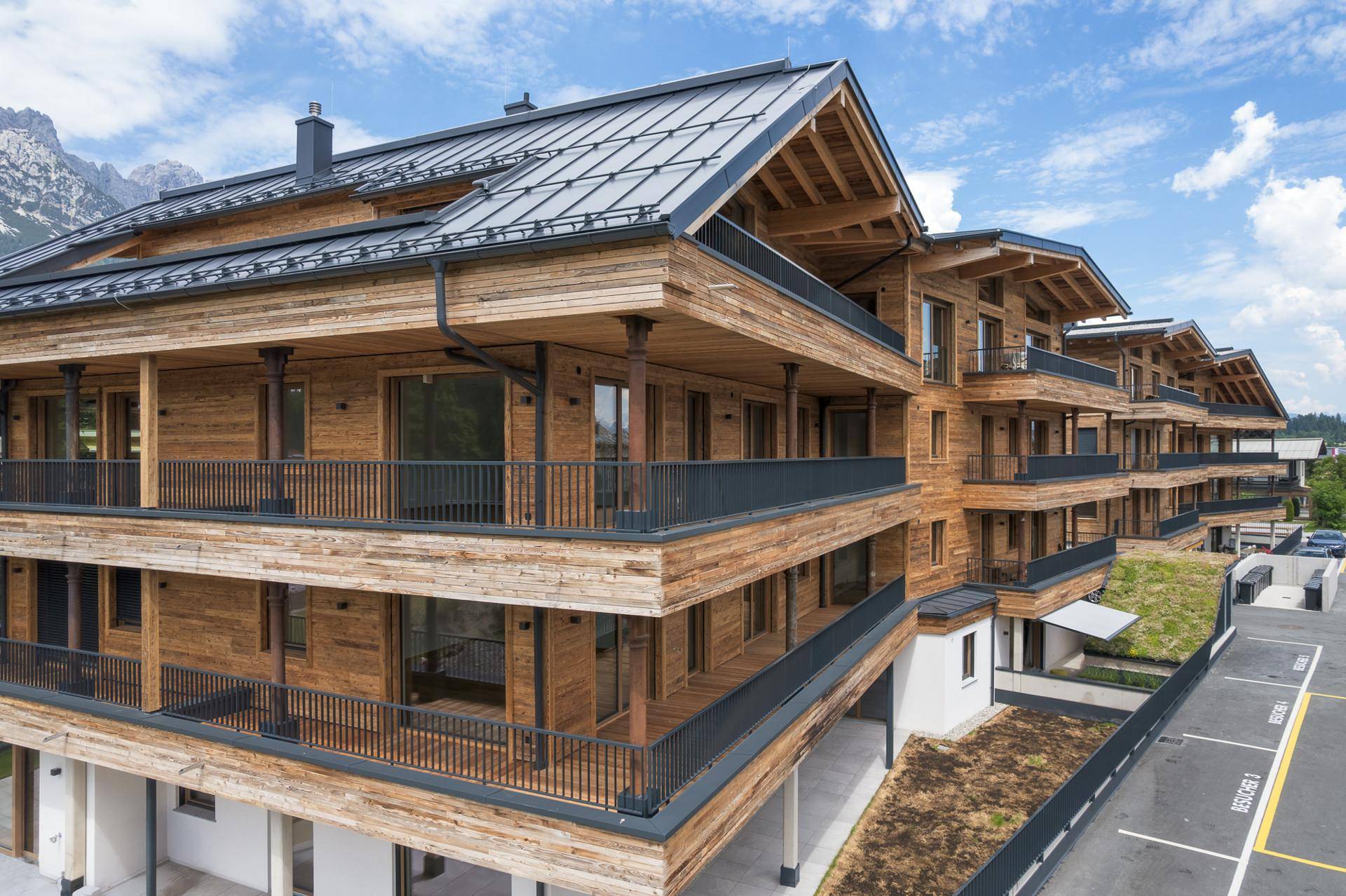 Detailansicht der modernen Holzfassade mit Balkonen und traditionellem Satteldach in alpiner Umgebung.