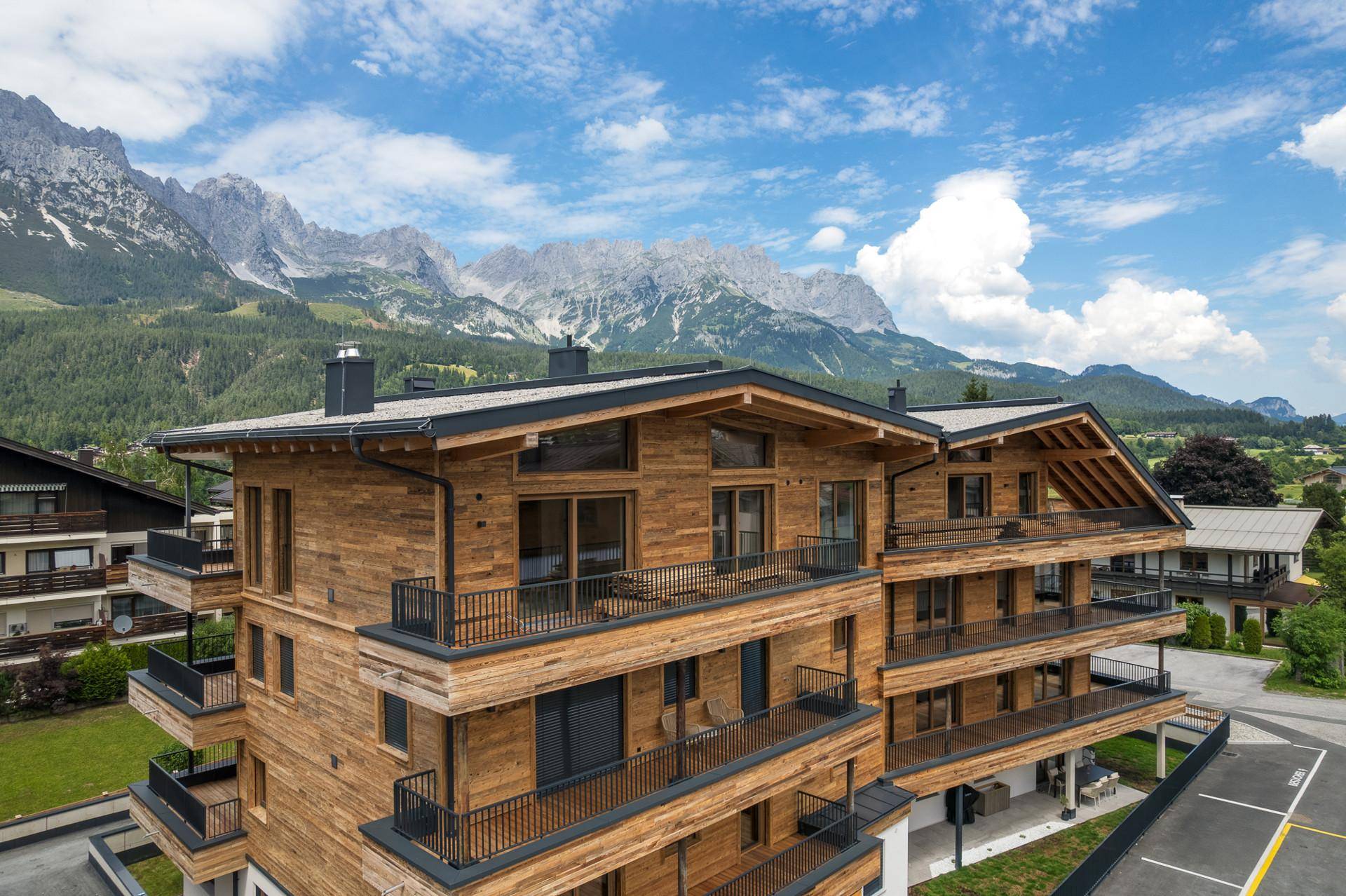 Ansicht der modernen Holzfassade mit großen Fenstern und Balkonen, eingebettet in die Berglandschaft.