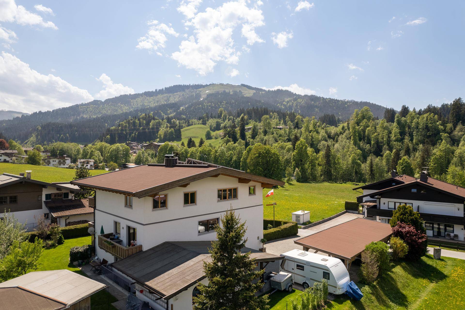 Weitläufiger Blick über grüne Wiesen und bewaldete Hügel mit einzelnen Häusern in der Ferne.