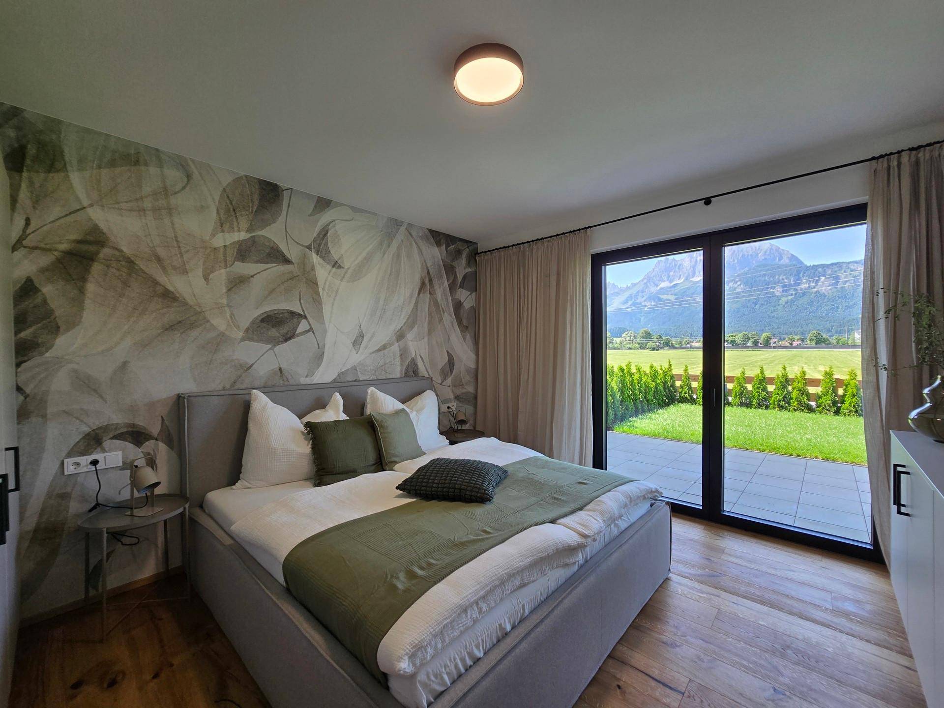 Gemütliches Schlafzimmer mit großem Bett, Holzboden und Zugang zur Terrasse mit Bergblick.