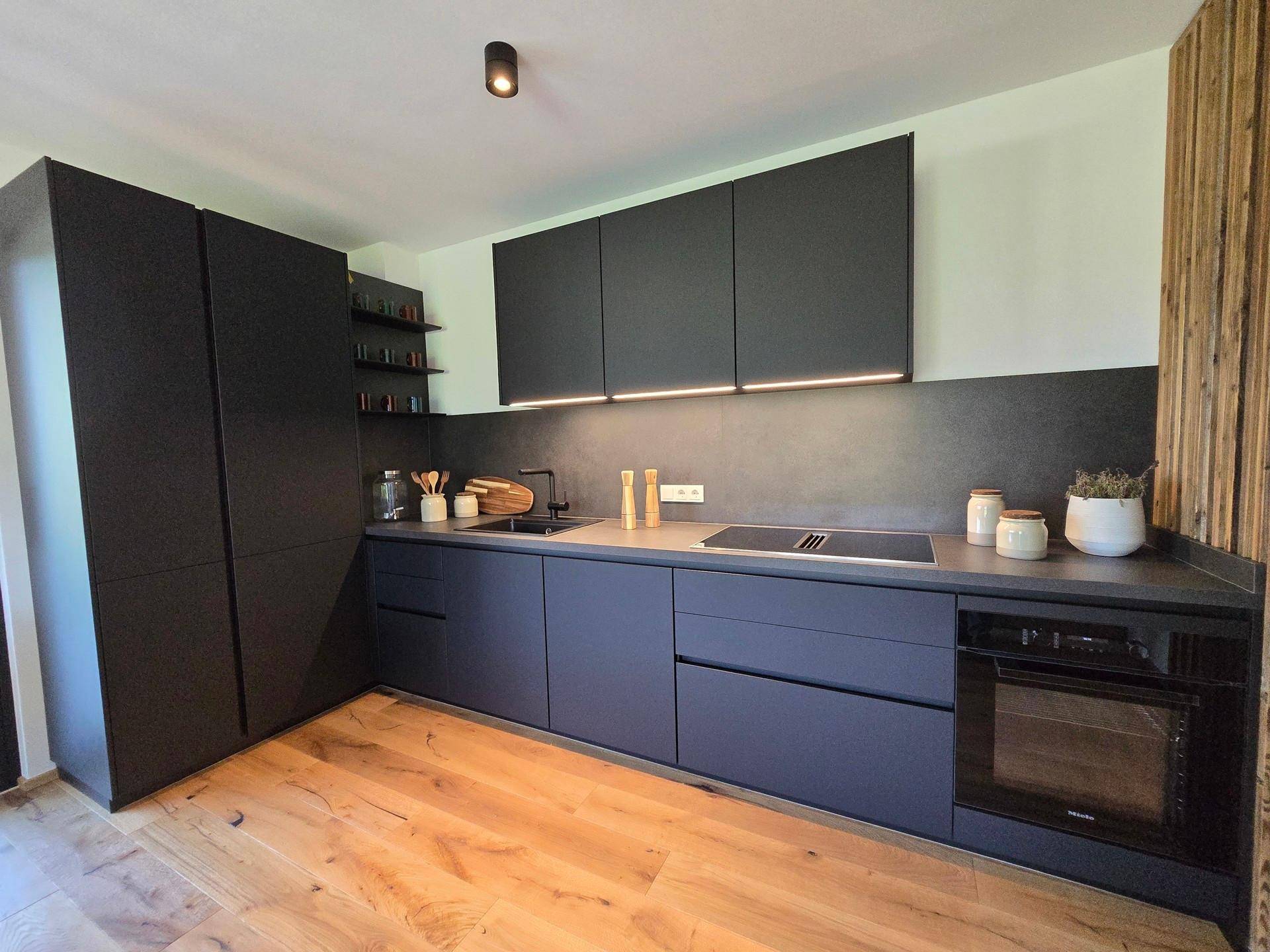 Moderne, minimalistische Küche in Schwarz mit integrierten Geräten und Holzboden.