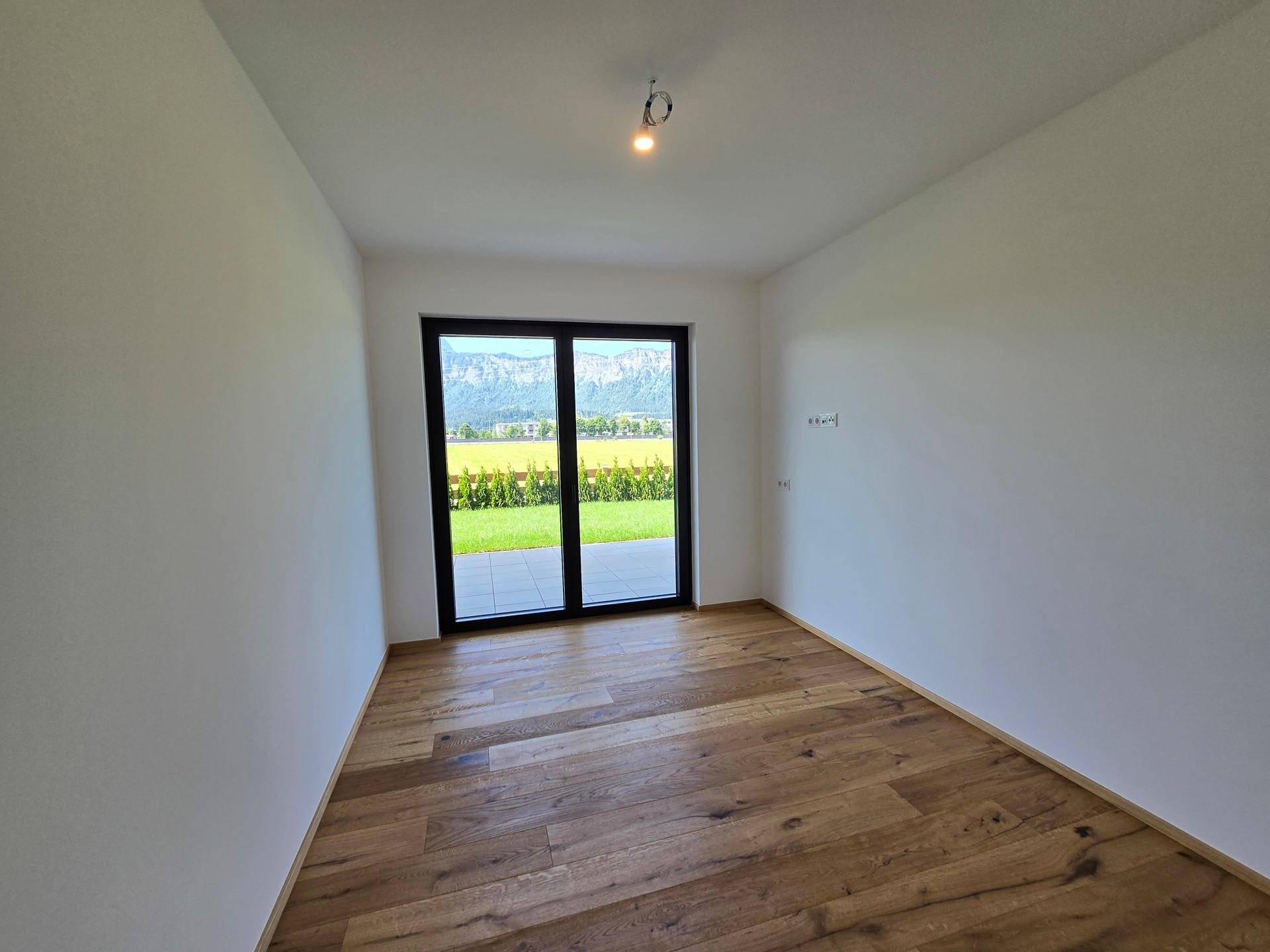 Leerer Raum mit Holzboden und großen Fenstern, die viel Tageslicht hereinlassen.