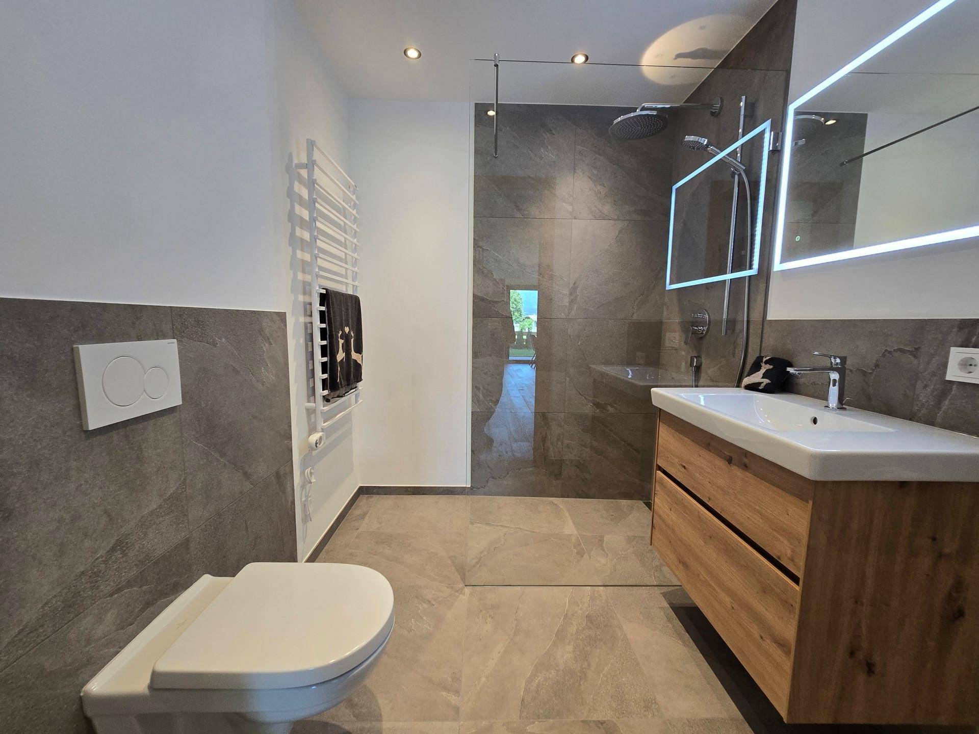 Modernes Badezimmer mit begehbarer Dusche, Holzwaschtisch und grauen Fliesen.