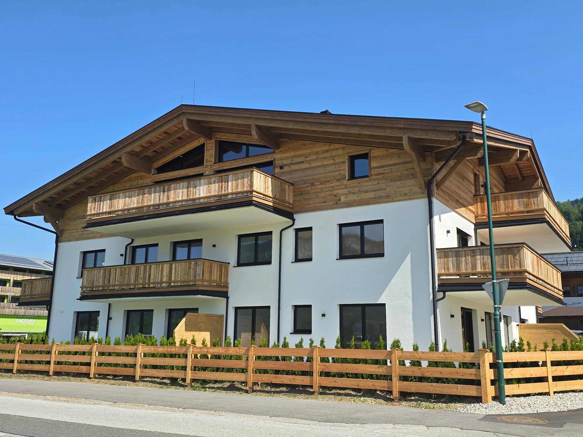 Ansicht des modernen Neubaus im alpinen Stil mit Holzbalkonen und gepflegter Umgebung.