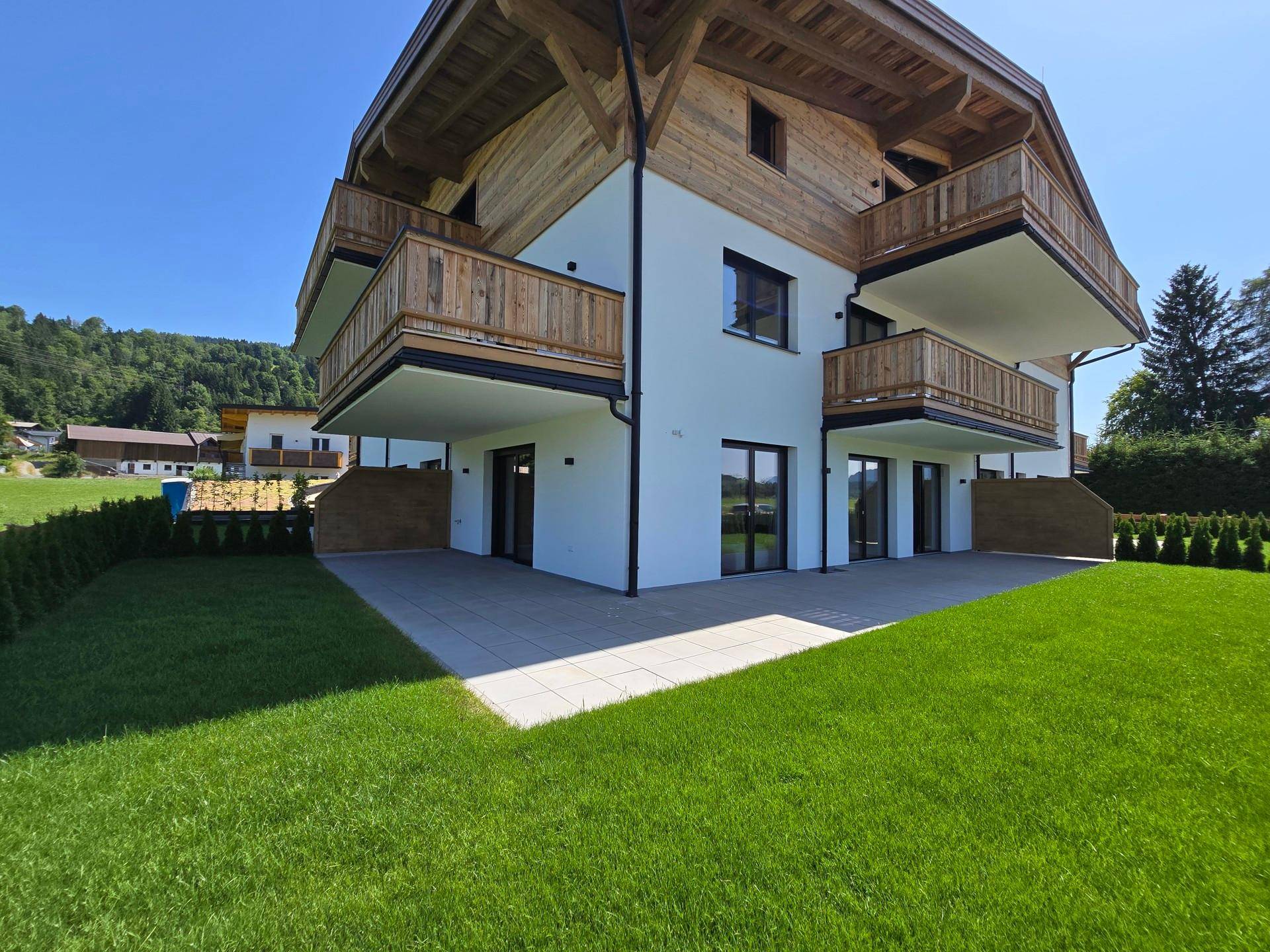 Gepflegter Gartenbereich mit Terrasse und Blick auf das moderne Gebäude im alpinen Stil.
