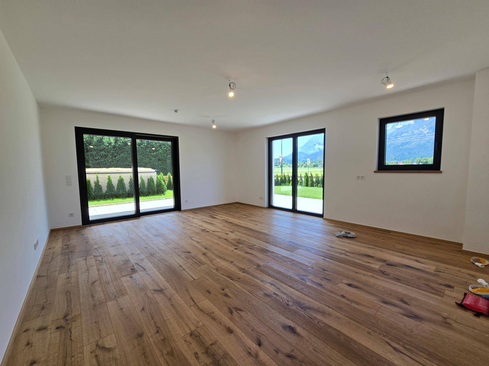 Heller, leerer Wohnraum mit Holzboden und großen Schiebetüren zum Garten.