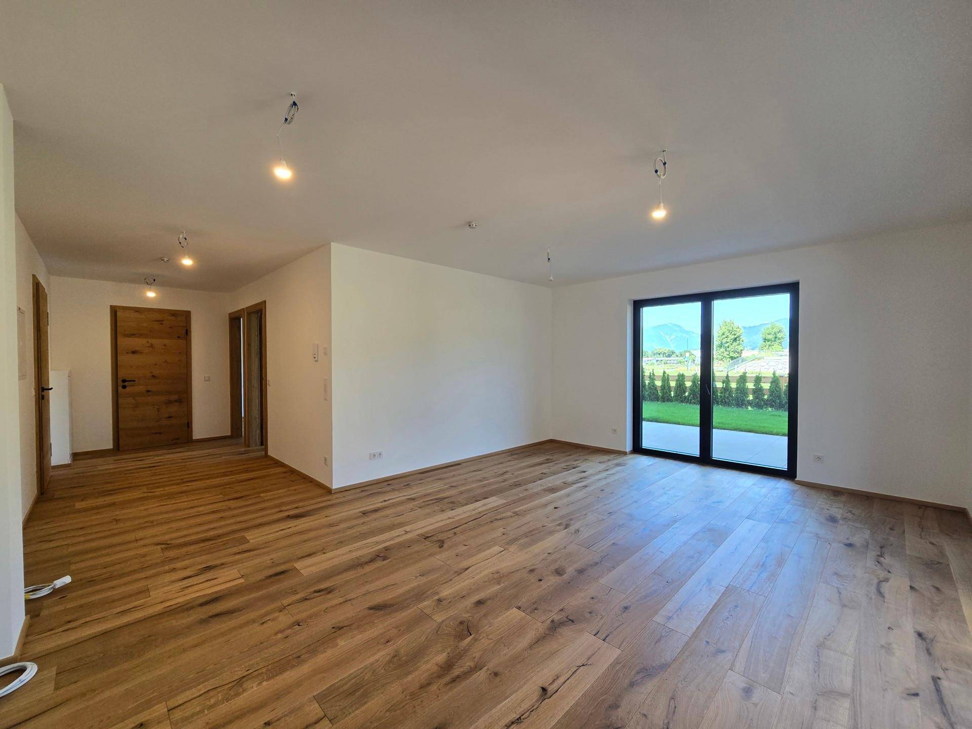 Geräumiger, unmöblierter Wohnbereich mit Holzboden und viel Tageslicht durch große Fenster.