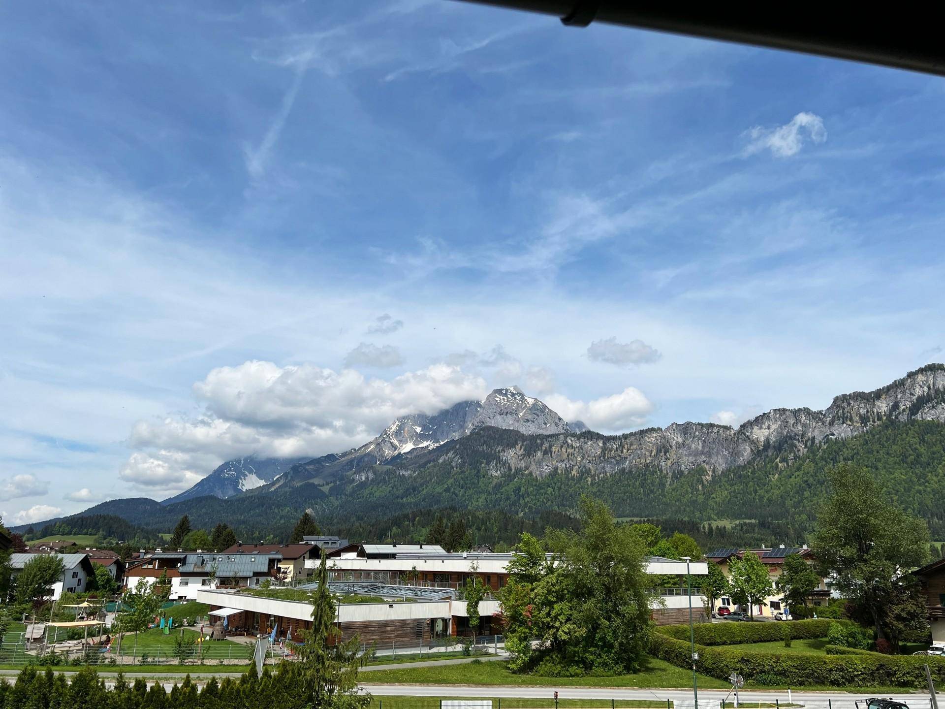 Malerischer Ausblick auf die majestätischen Berge, grüne Landschaft und ein charmantes Dorf unter blauem Himmel.