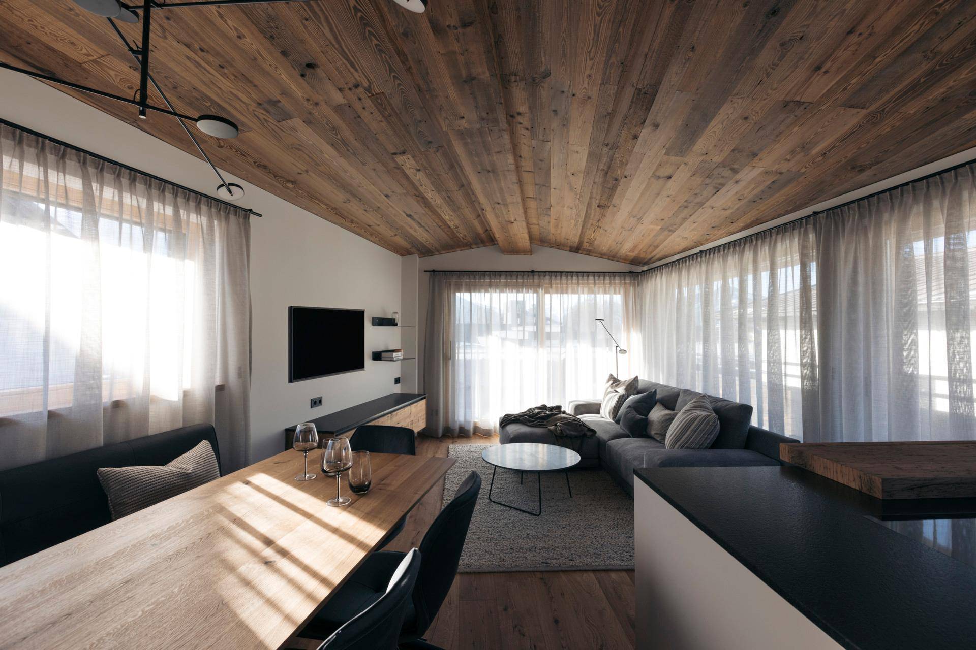 Gemütlicher Wohnbereich mit Holzbalkendecke, bequemer Couch und Esstisch, durchflutet von natürlichem Licht.