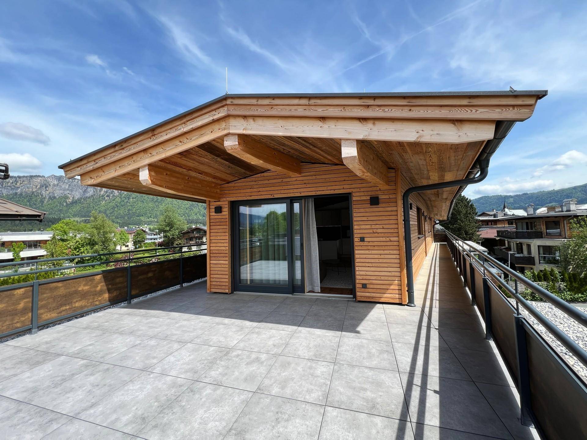 Großzügige Dachterrasse mit Holzelementen, Fliesenboden und weitem Blick auf die umliegende Berglandschaft.
