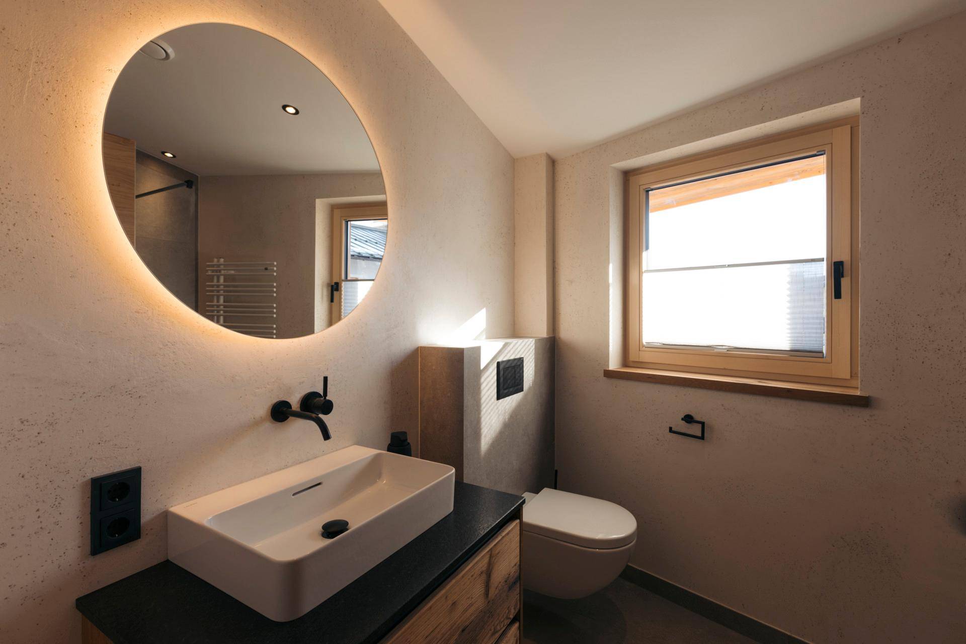Elegantes Badezimmer mit beleuchtetem Spiegel, modernem Aufsatzwaschbecken und wandhängendem WC.
