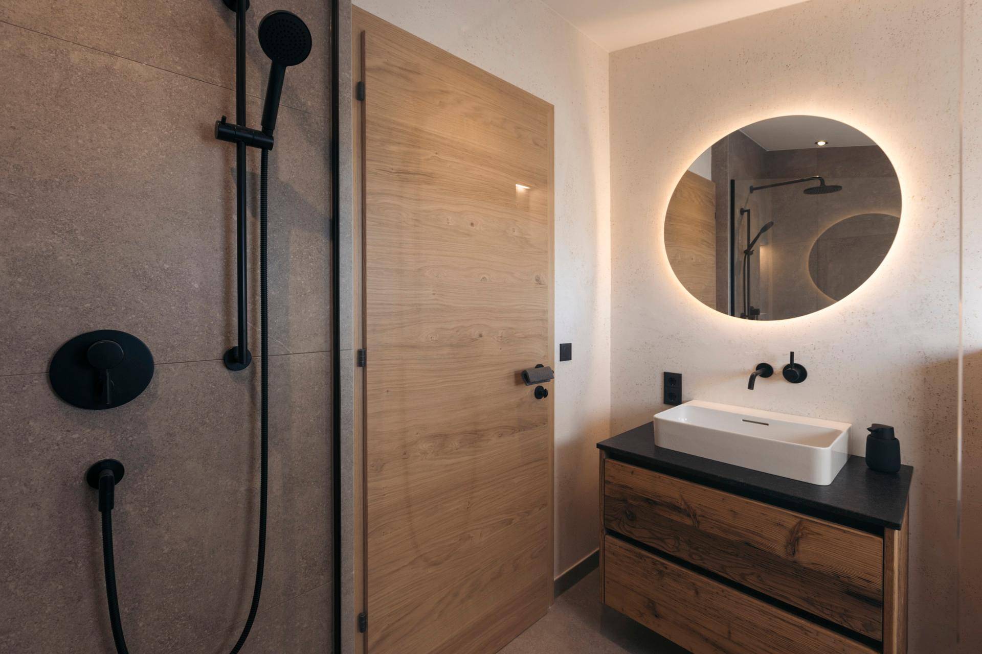 Stilvolles Badezimmer mit begehbarer Dusche, Holzwaschtisch und einem runden, beleuchteten Spiegel.