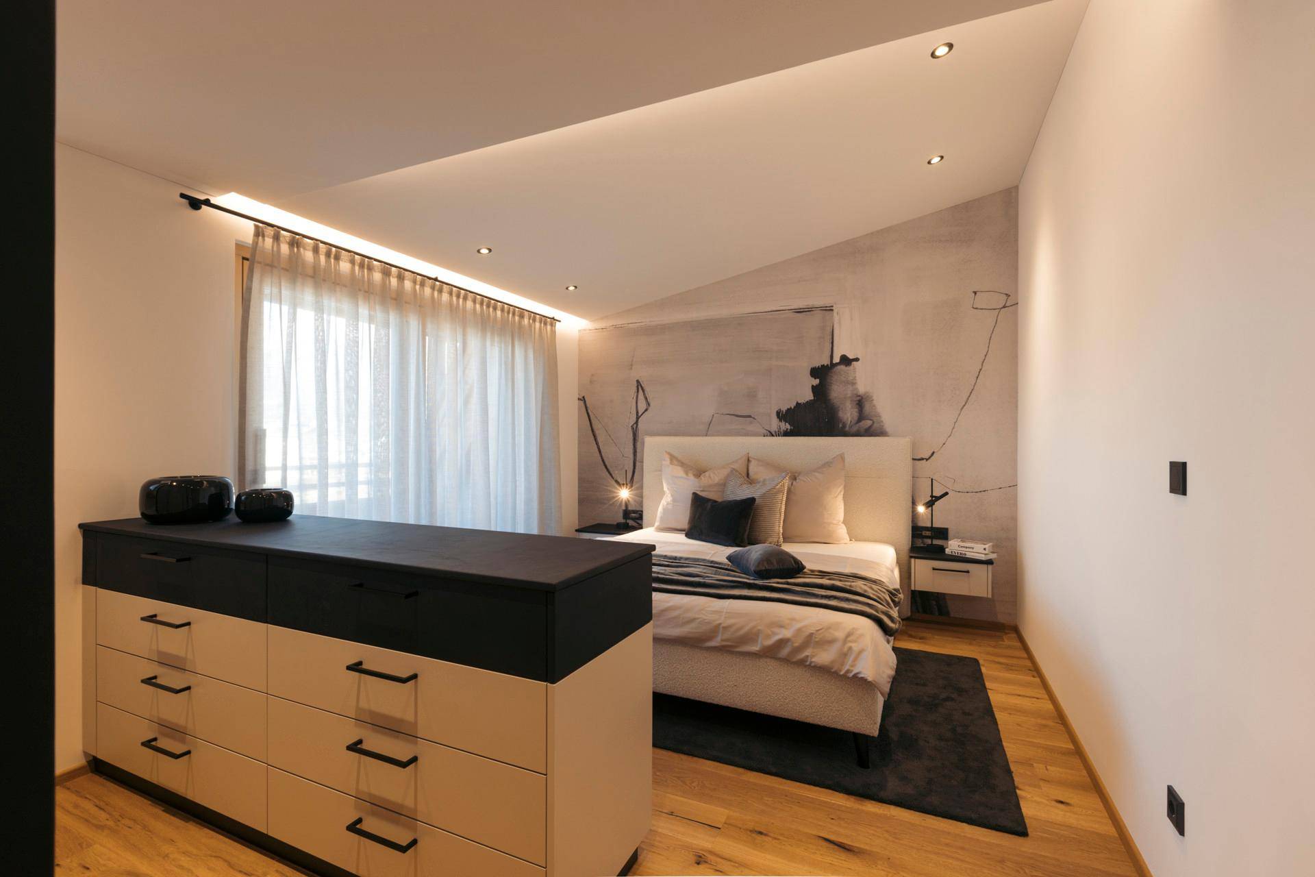 Geräumiges Schlafzimmer mit Dachschräge, Holzboden und einem großen Fenster, das viel Tageslicht hereinlässt.
