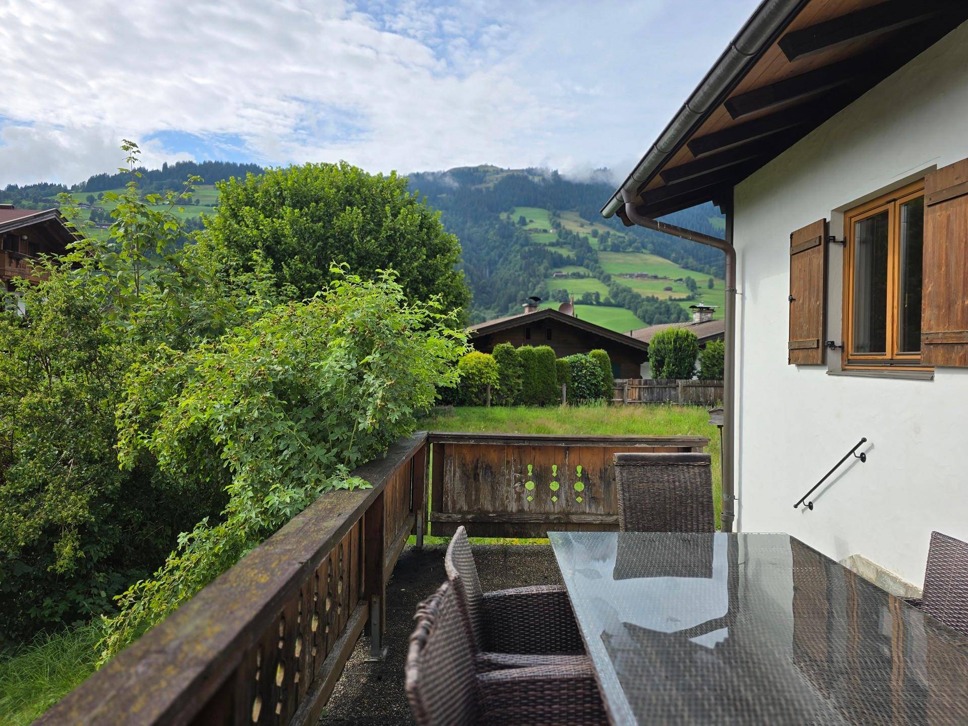 Geräumige Holzterrasse mit Glas-Esstisch und Korbstühlen, ideal für Mahlzeiten im Freien.