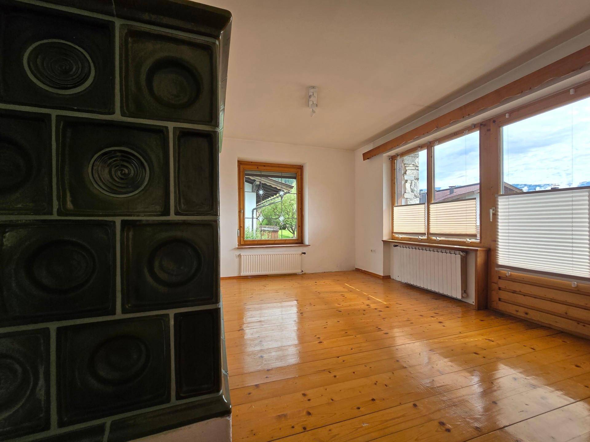 Gemütliches Wohnzimmer mit traditionellem Kachelofen, Holzboden und großen Fenstern, sehr hell.