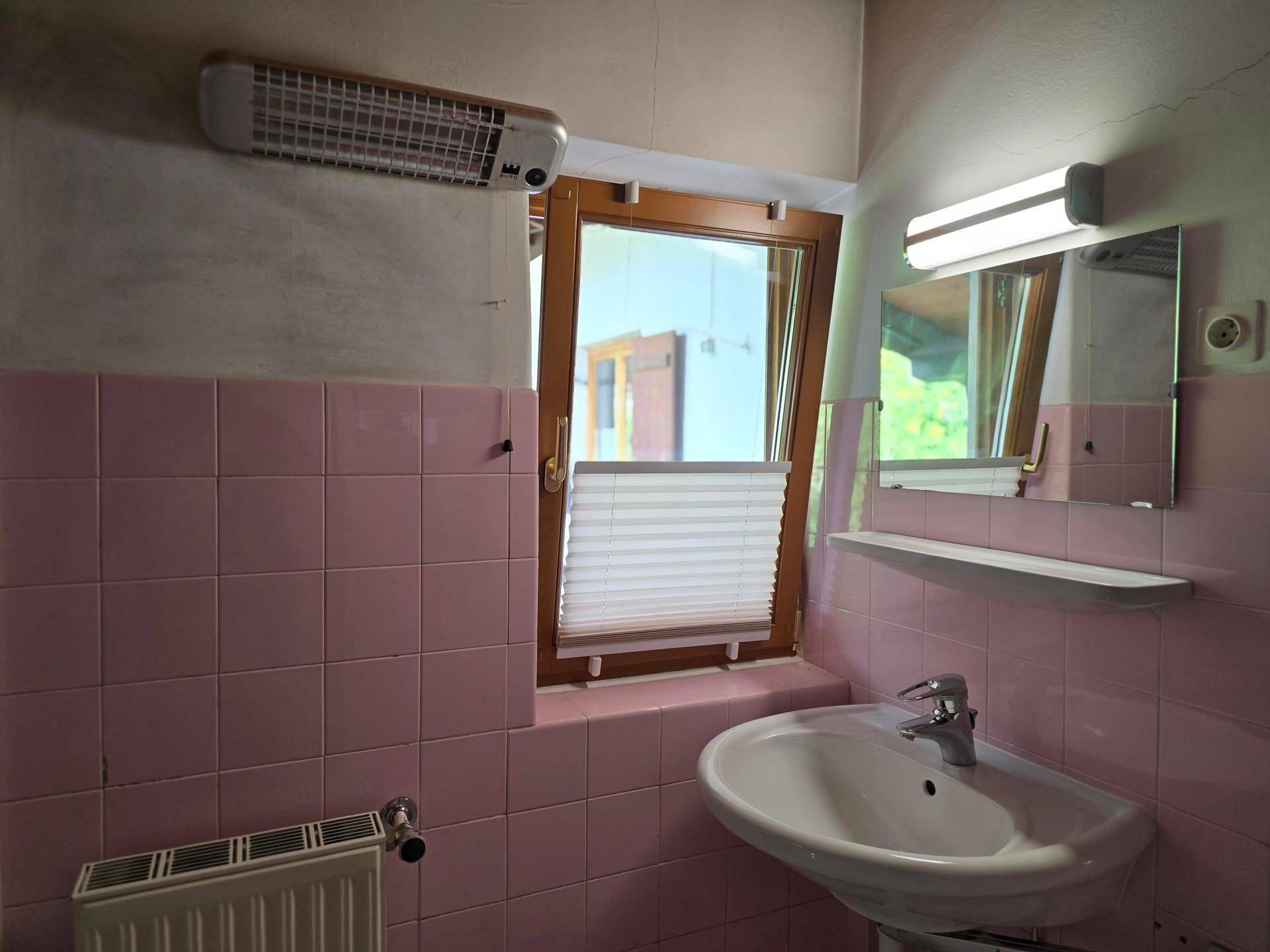 Badezimmer mit rosa Fliesen, Waschbecken und Fenster, das Tageslicht hereinlässt, im 80er-Jahre-Stil.