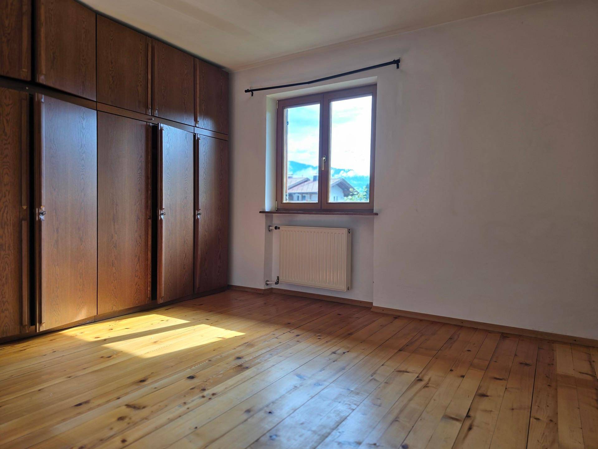 Schlafzimmer mit Holzboden, großen Einbauschränken und Fenster mit Bergblick, sehr geräumig.