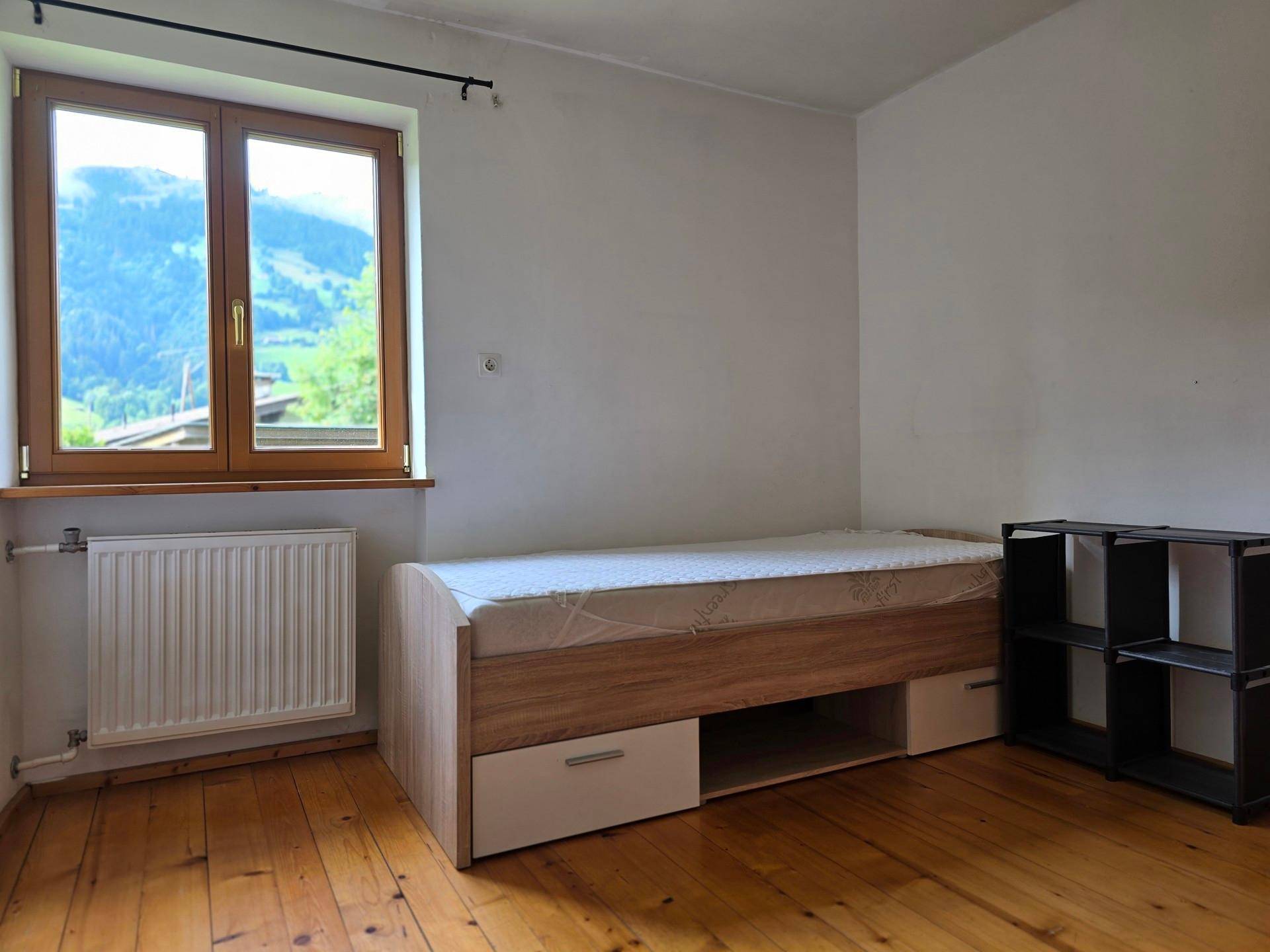Schlafzimmer mit Einzelbett und Stauraum, Holzboden und Fenster mit Bergblick, funktional eingerichtet.