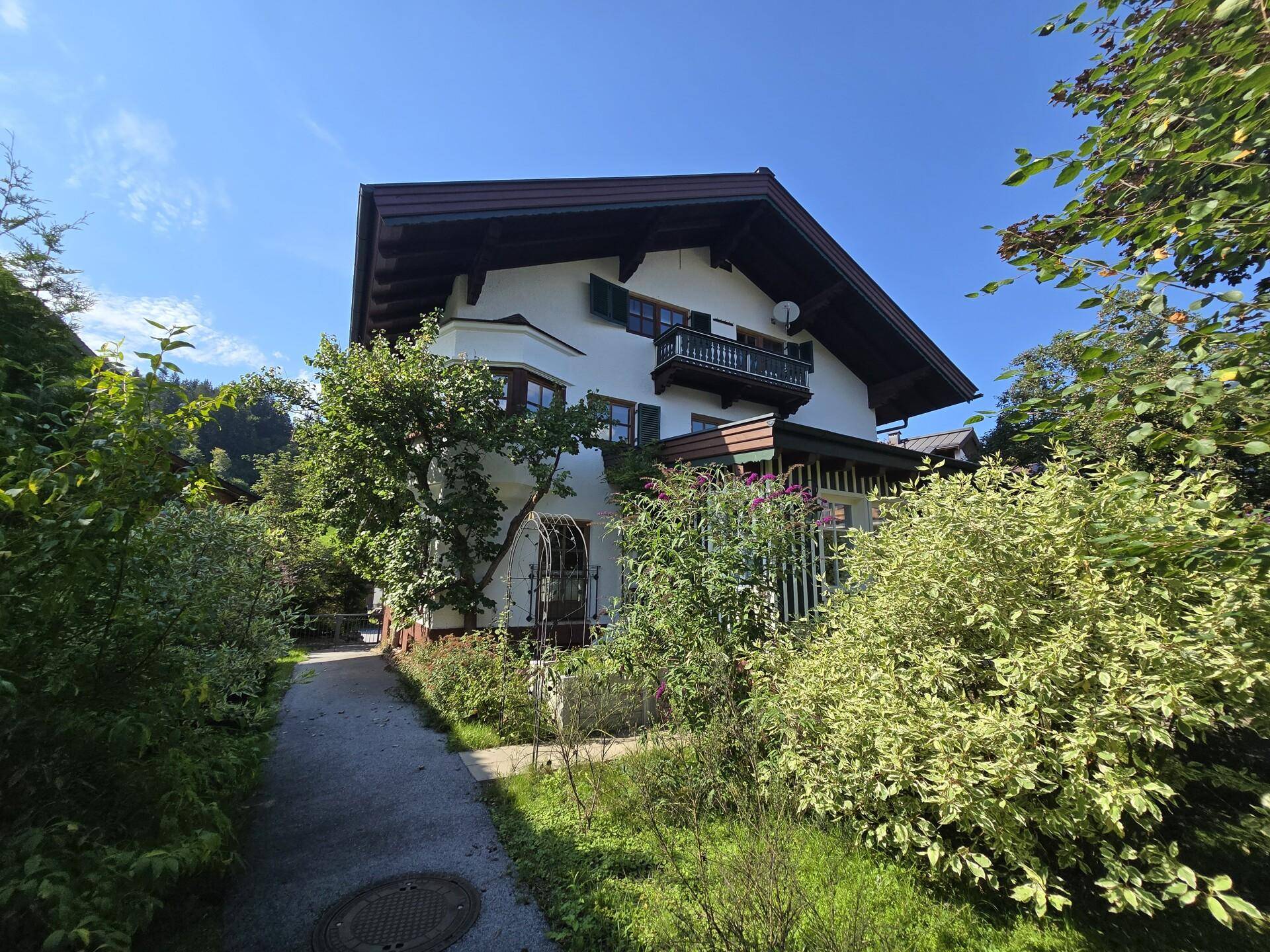 Charmantes Haus mit üppiger Bepflanzung und einem schmalen Gartenweg unter blauem Himmel.
