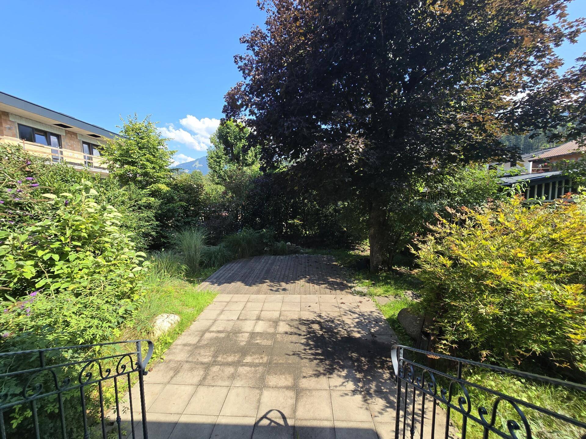 Gepflegter Gartenbereich mit Steinplattenweg und üppiger grüner Bepflanzung unter blauem Himmel.
