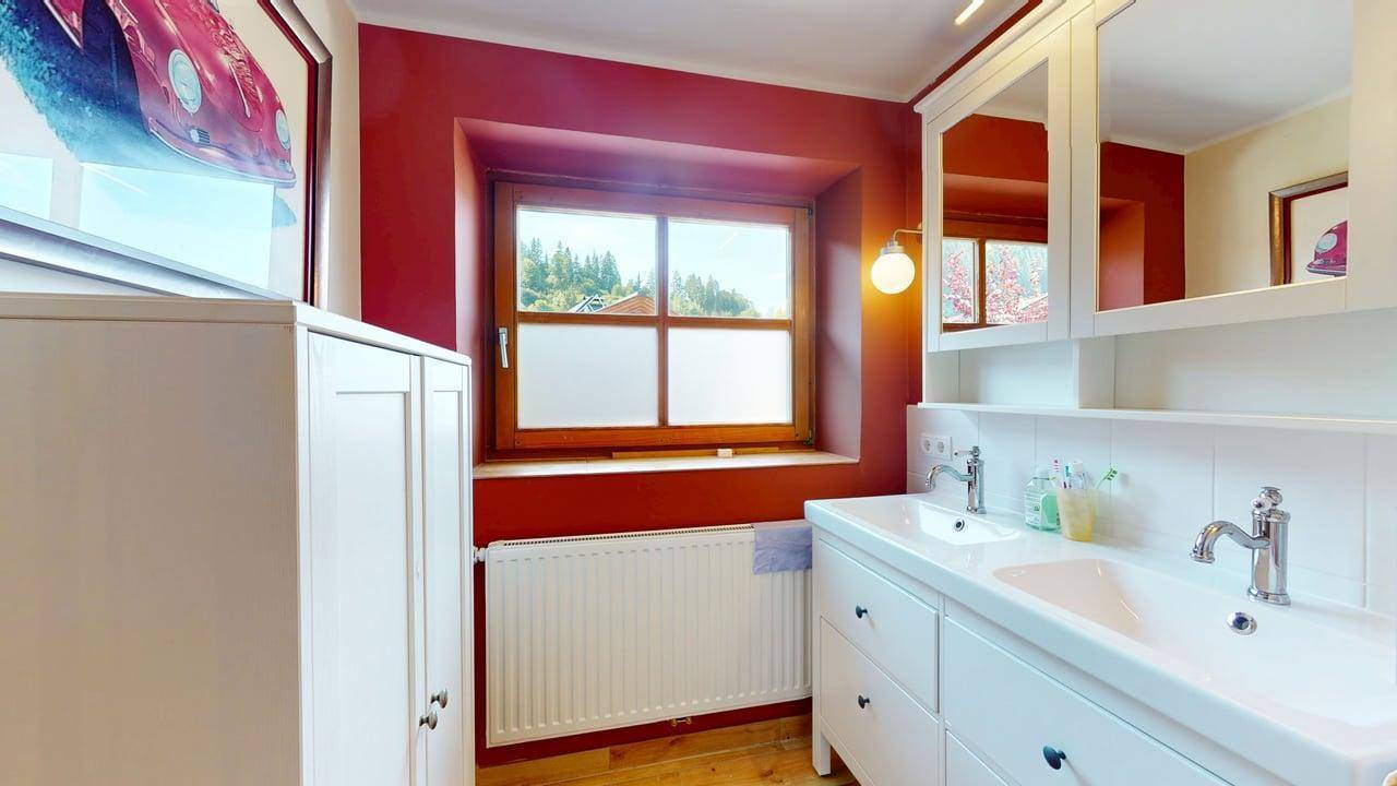 Modernes Badezimmer mit Doppelwaschbecken, weißen Möbeln und Fenster mit Blick ins Grüne.