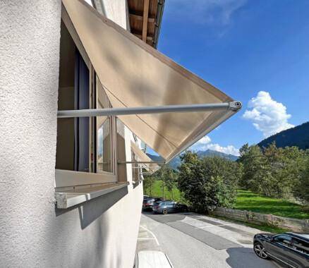 Fenster mit ausgefahrener Markise an der Fassade eines Gebäudes mit Blick auf die Berge.