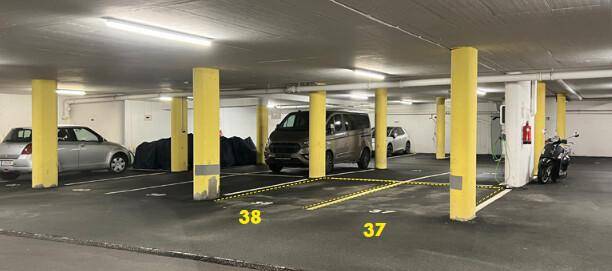Tiefgarage mit mehreren Stellplätzen, gelben Säulen und Beleuchtung.