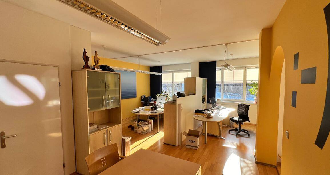 Bürofläche mit gelben Wänden, Holzboden und Arbeitsplätzen, die durch Trennwände separiert sind.