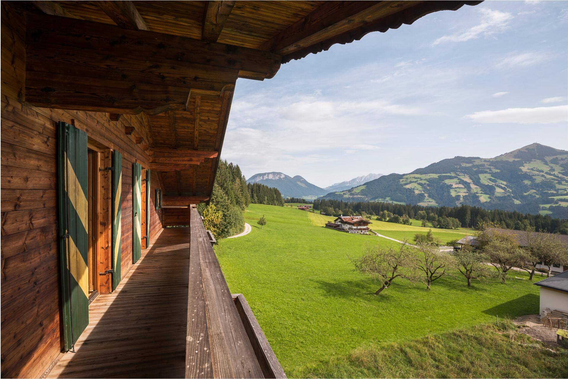 Langer Holzbalkon mit idyllischem Ausblick auf grüne Wiesen und die majestätischen Berge.
