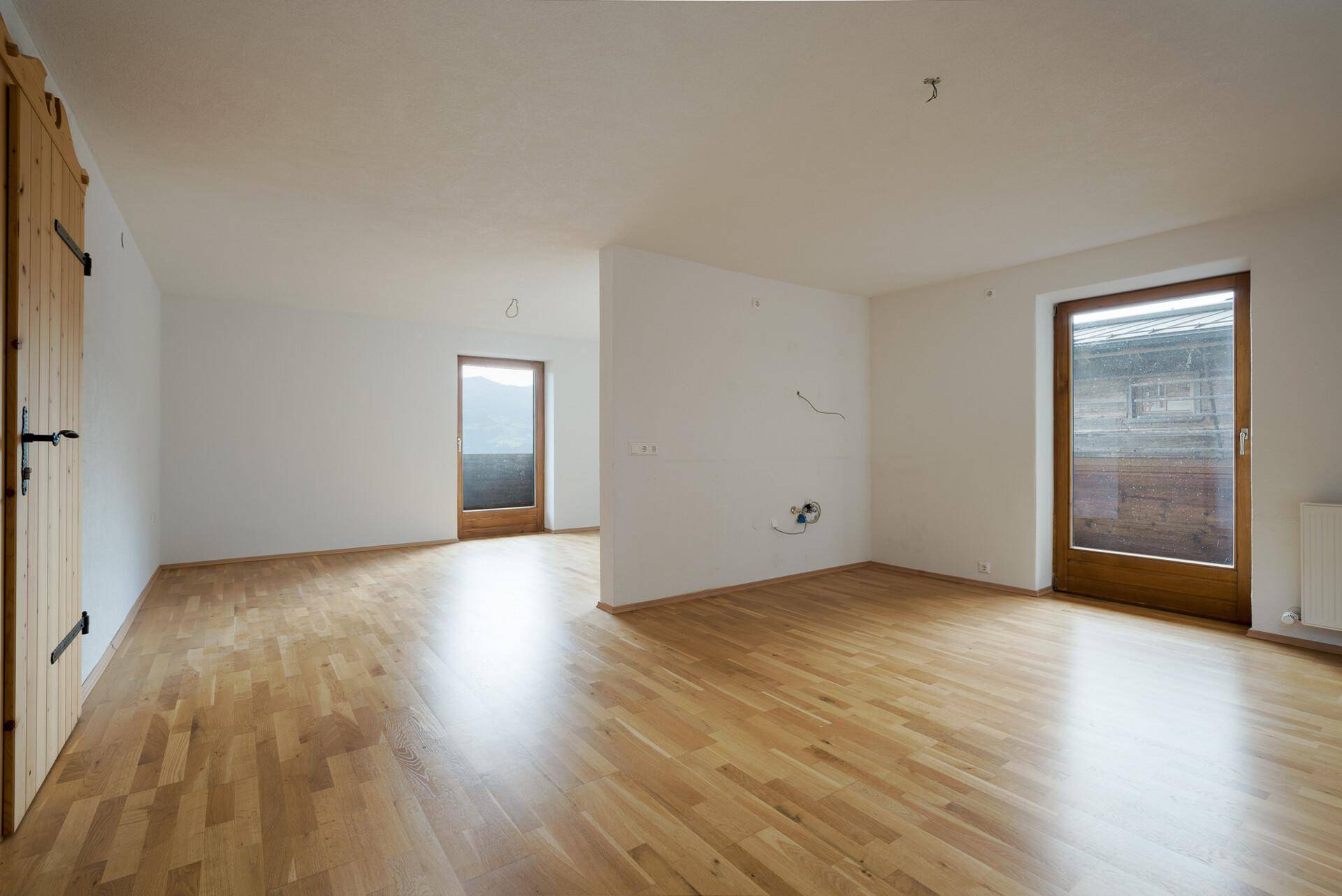 Geräumiger, leerer Raum mit hellem Holzfußboden und Zugang zu einem Balkon oder Terrasse.