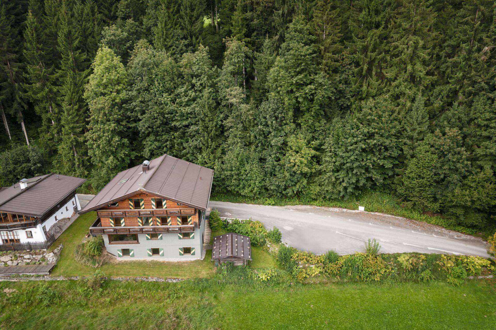 Luftaufnahme des Alpenhauses mit Satteldach und umliegender Landschaft, umgeben von Wald und Wiesen.
