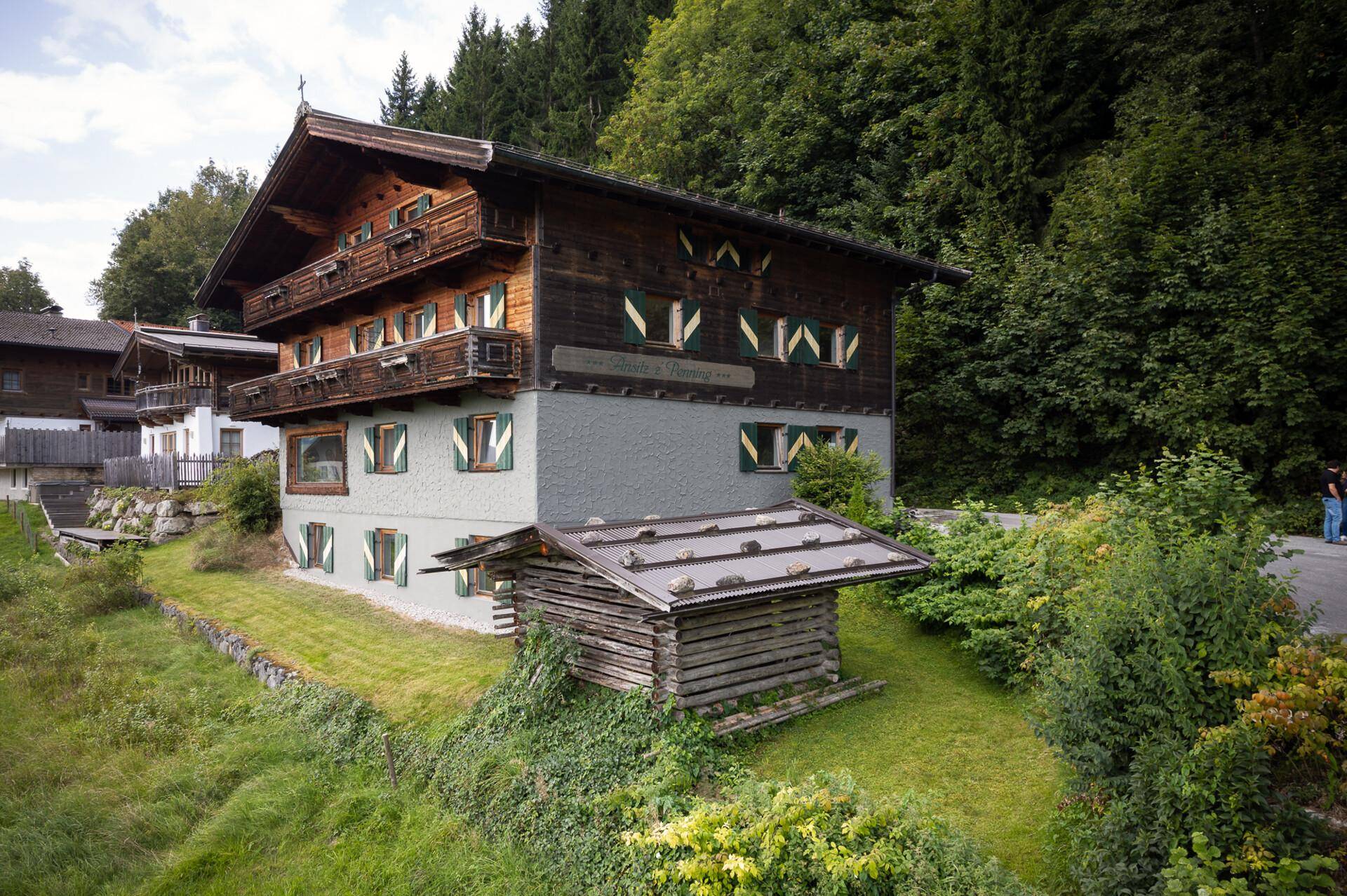 Traditionelles Alpenhaus mit Holzbalkonen und einem kleinen Holzschuppen, eingebettet in die Natur.