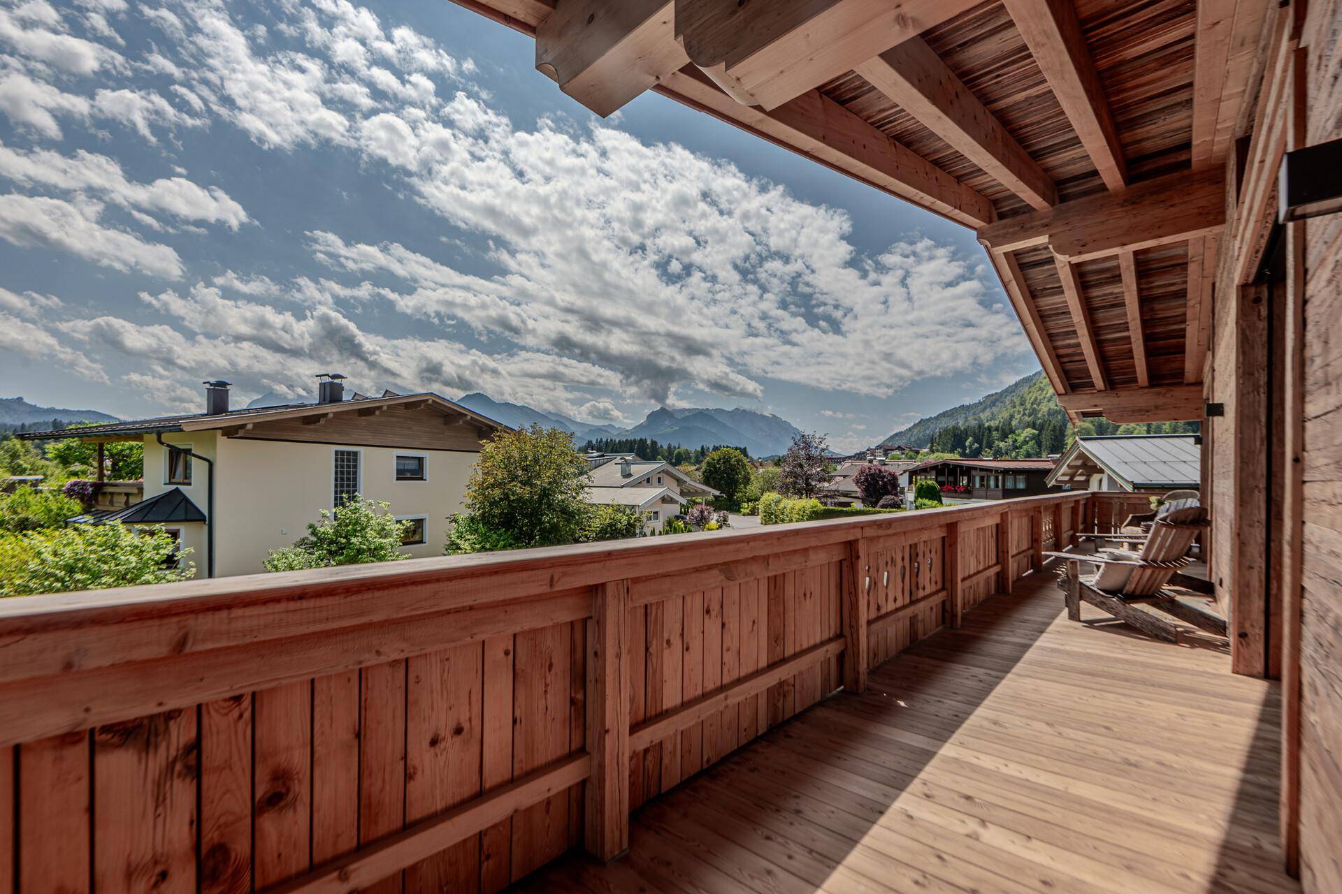 Langer Holzbalcon mit traditionellem Geländer und beeindruckendem Blick auf die umliegenden Berge.