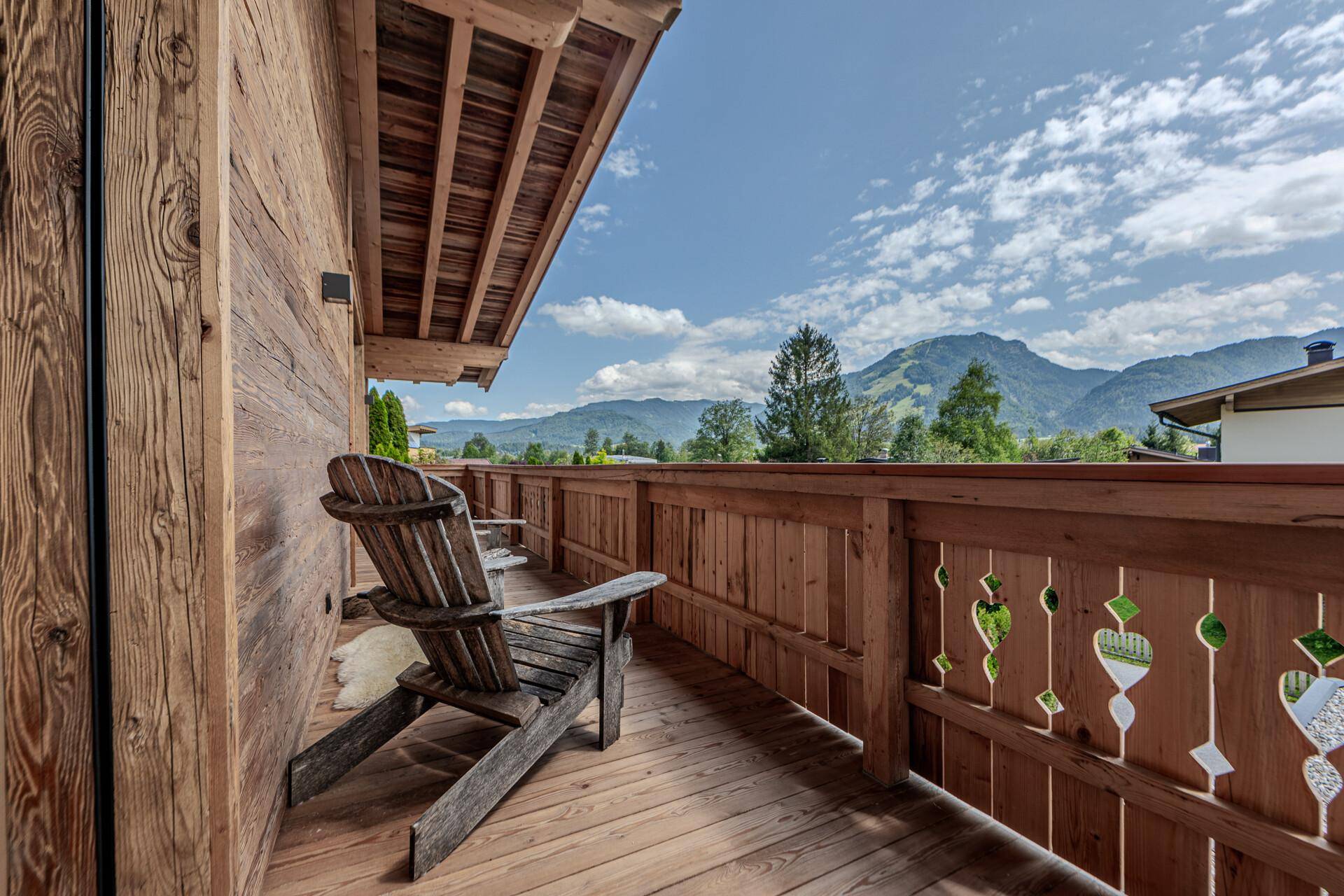 Traditioneller Holzbalcon mit rustikalem Sessel und weitem Blick über die grüne Berglandschaft.