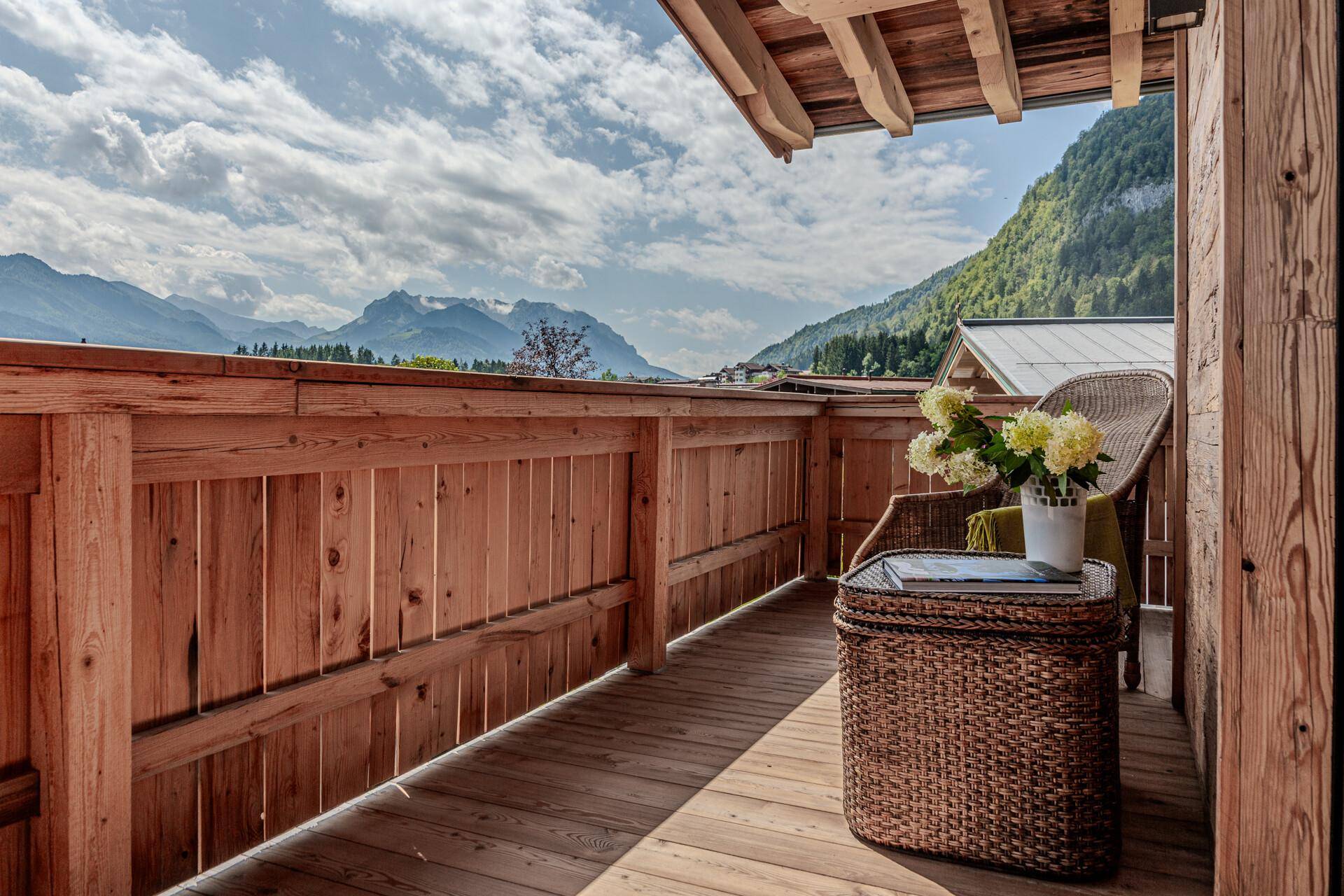 Gemütlicher Holzbalcon mit Korbsessel und einem atemberaubenden Panoramablick auf die Berge.